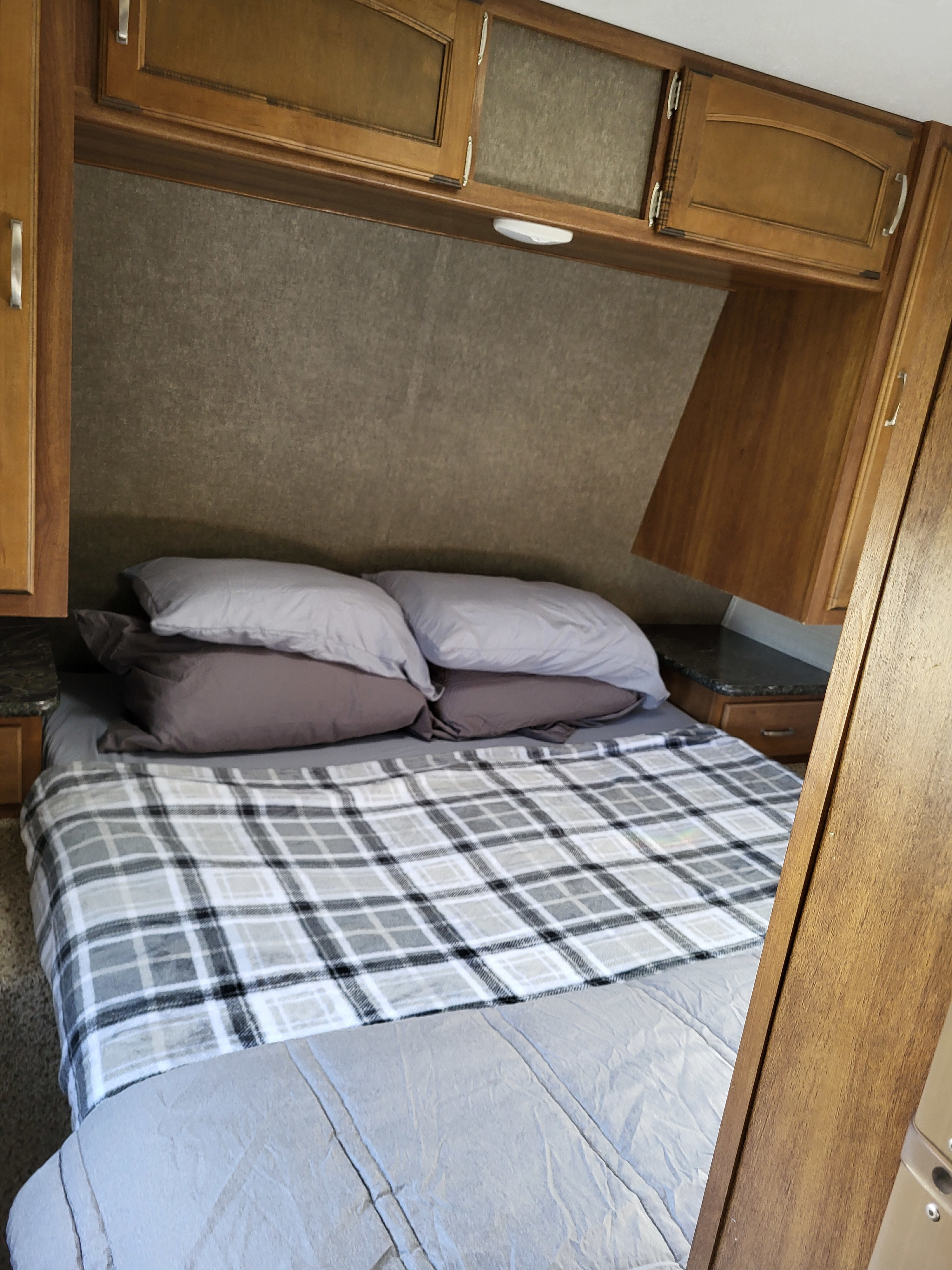 Cozy RV rental bedroom featuring a comfy bed with a plaid blanket, overhead wood cabinets, and side nightstands.. Keystone RV Springdale 2017