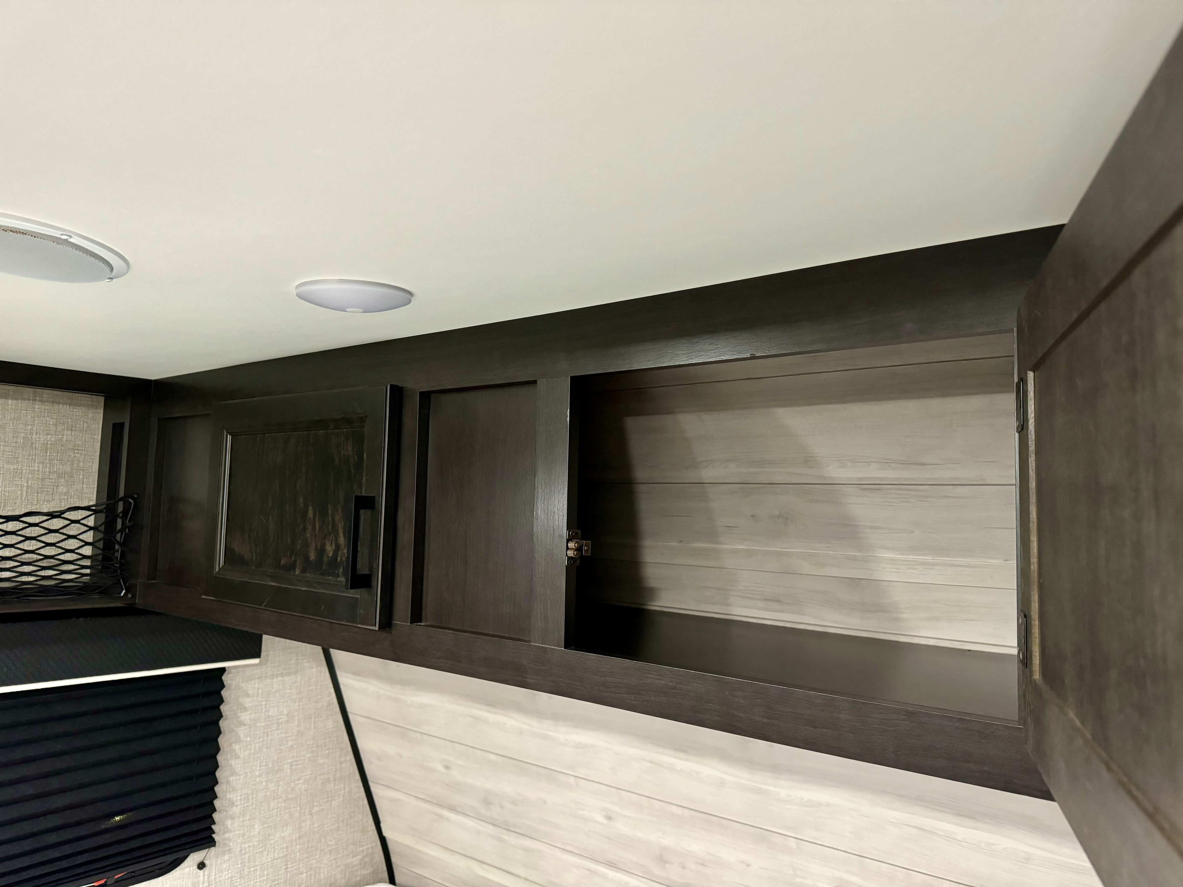 RV rental: Interior view showing sleek dark overhead cabinets, one open for storage, with modern ceiling lights and light wood walls.. Jayco Jay Flight SLX 2022