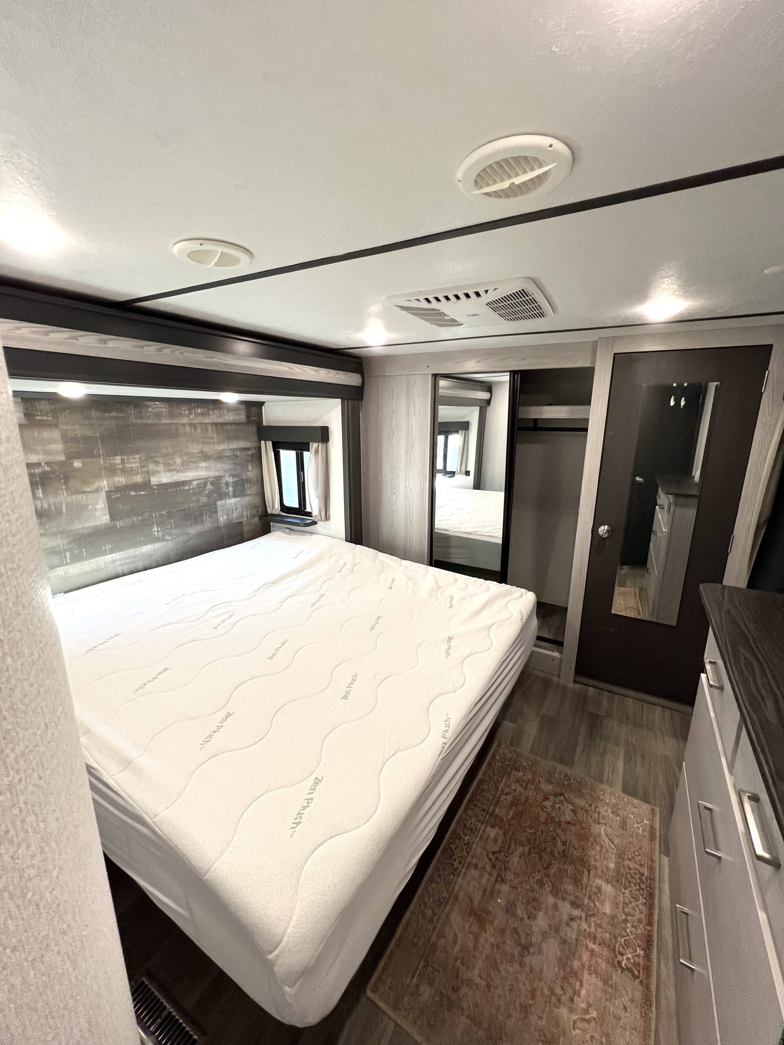 Spacious RV rental bedroom featuring a large Zen Plush mattress, wood-paneled wall, closet with mirrored doors, and dresser.. Keystone RV Montana High Country 2021