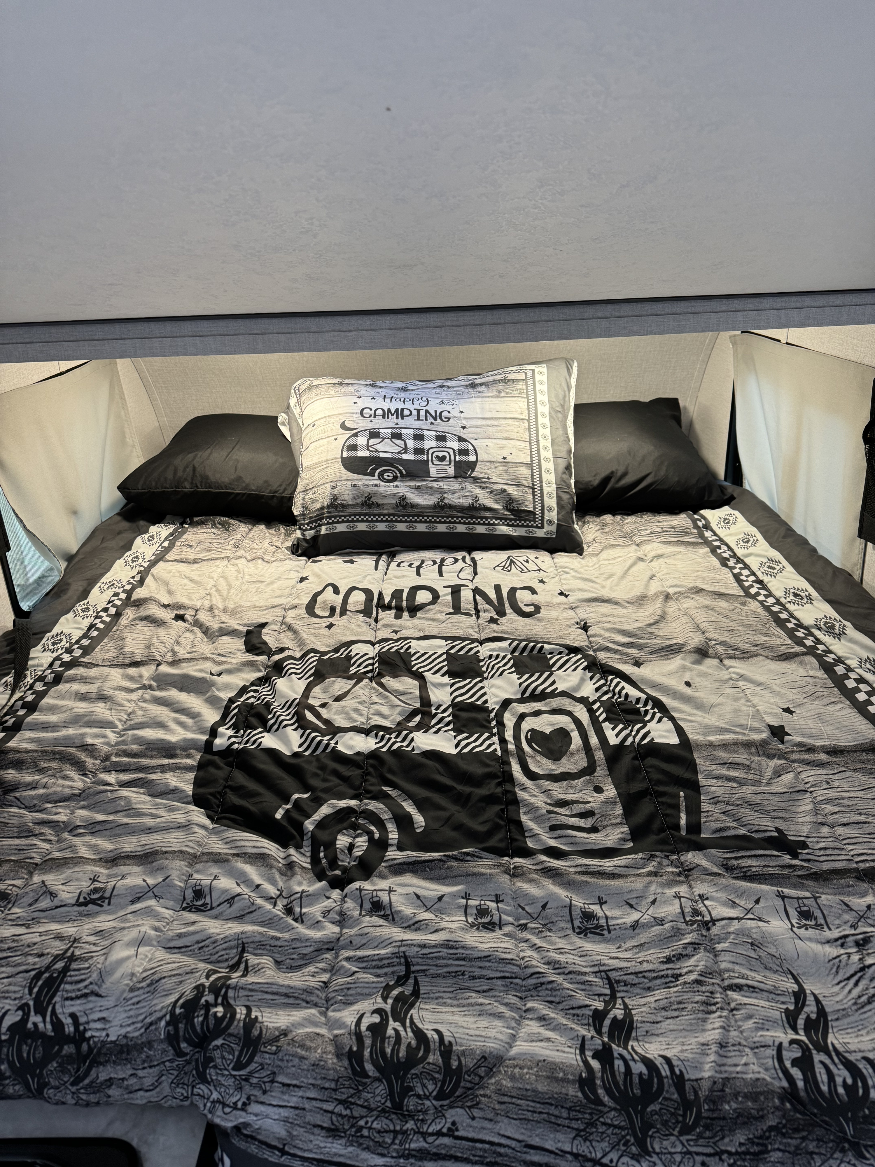 Cozy RV rental bed with "Happy Camping" comforter & pillow, featuring a black & white camper design.. Forest River Viking TD 2023