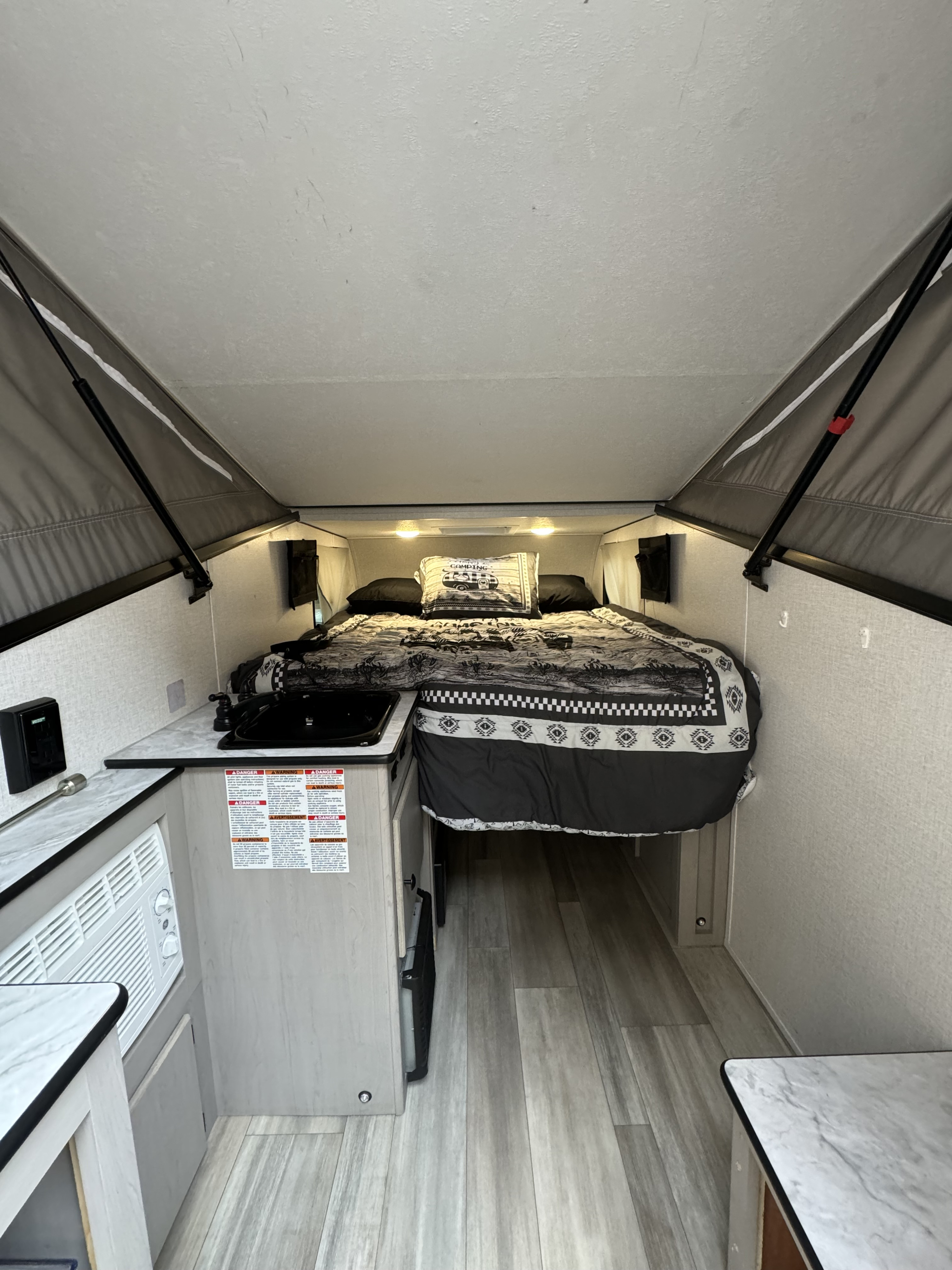 Inside a compact RV rental: a comfortable bed with themed bedding, small kitchen, and AC unit. Ready for camping trips.. Forest River Viking TD 2023