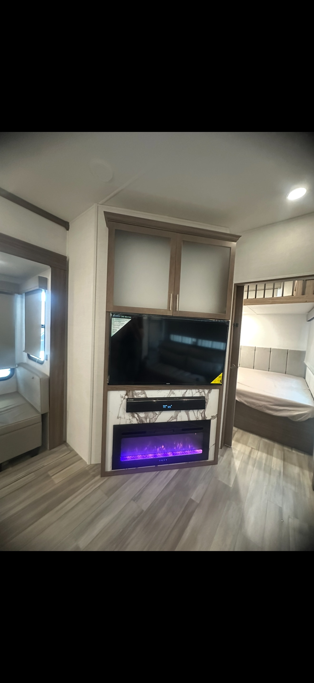 Modern RV rental living area featuring a TV, glowing purple electric fireplace, sleek cabinets, and a cozy bedroom.. Alliance RV Avenue 2024