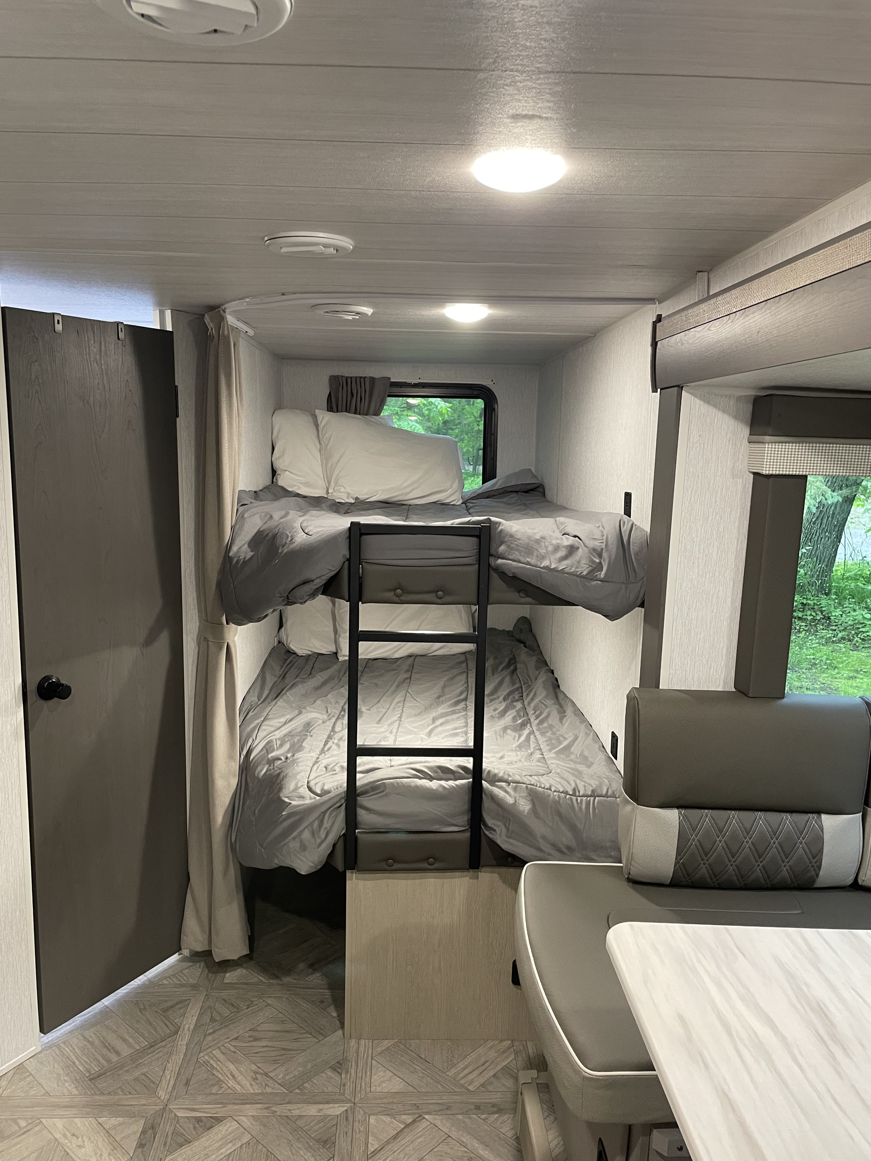 Cozy RV rental interior featuring bunk beds, a dining area, and stylish wood-look flooring.. Forest River Wildwood X-Lite Platinum 2024