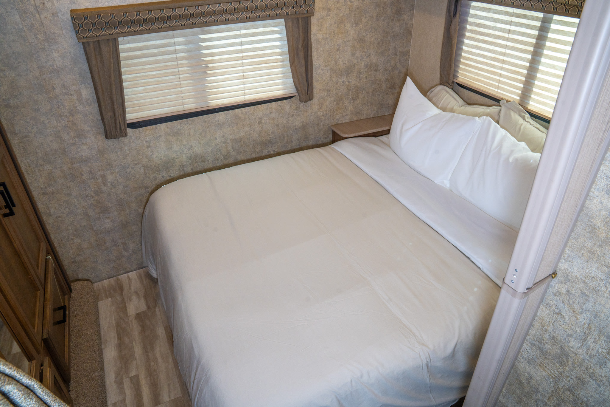 Experience comfort in this RV rental bedroom: a clean bed with white linens, two windows, and practical built-ins.. Gulf Stream Conquest 2019