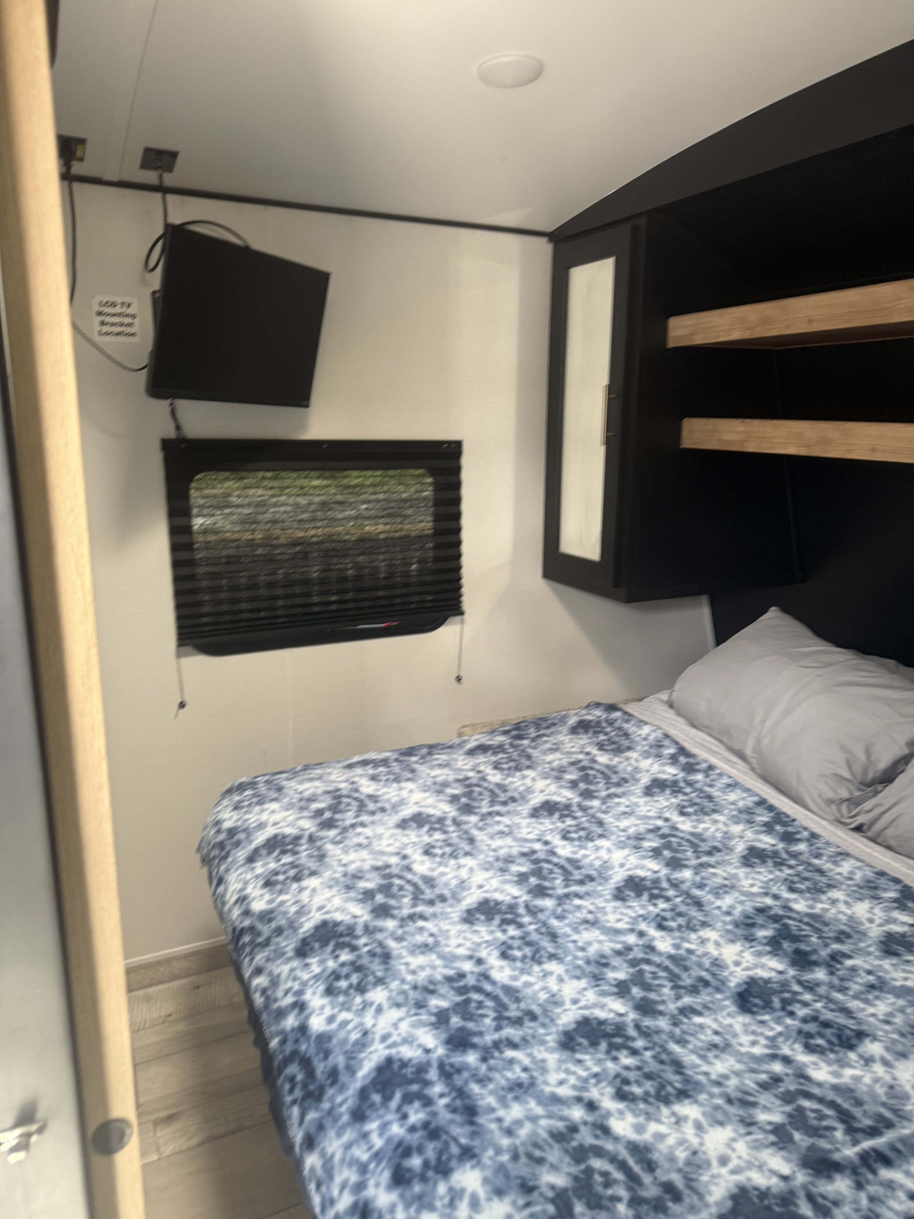 This RV rental features a well-appointed bedroom with a mounted TV, window, overhead storage, and a comfy bed.. Keystone RV Springdale 2022