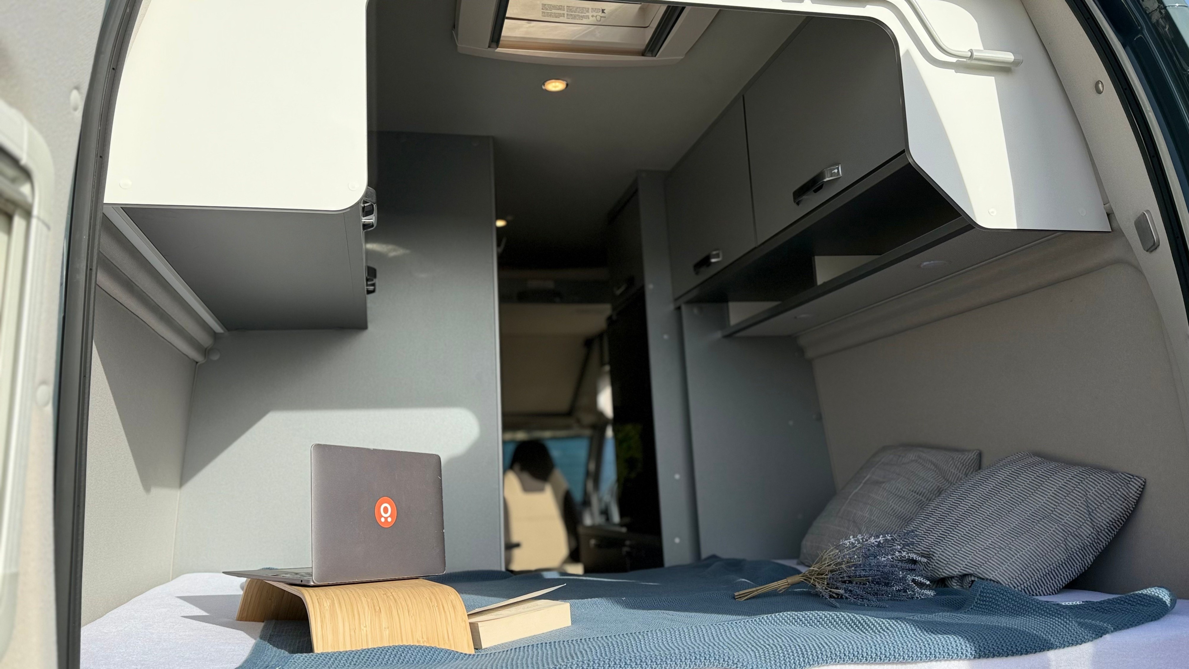 Cozy RV rental interior shows a comfy bed with a laptop, book, & lavender, ideal for digital nomads.. Weinsberg DQ 2024