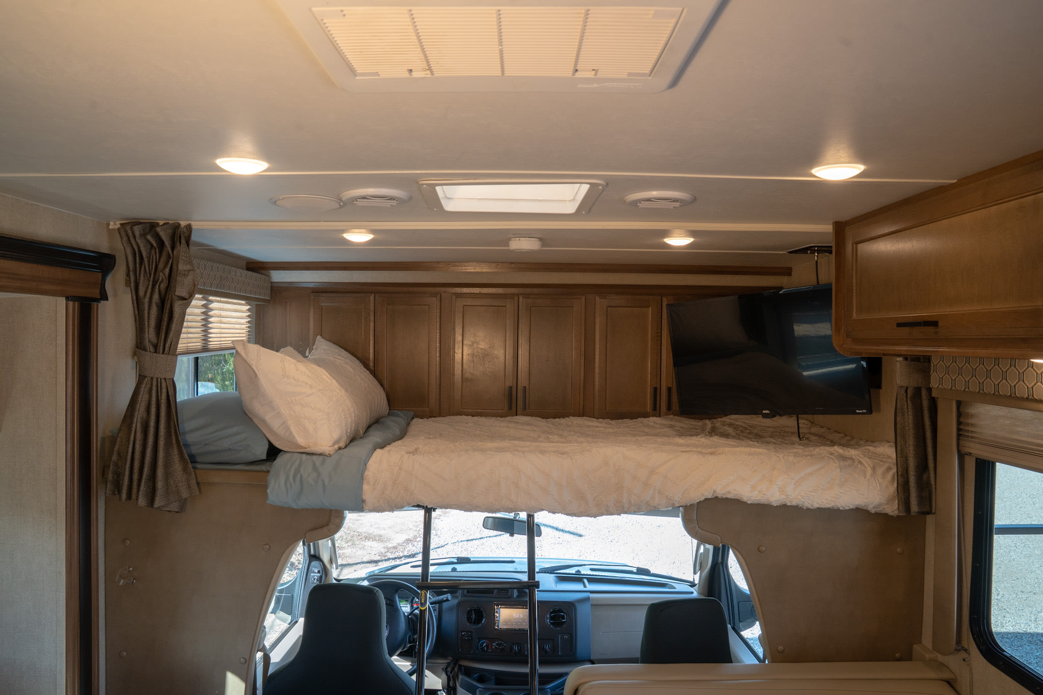 Interior of an RV rental: a spacious overhead bunk bed, accessible by ladder, above the front dashboard and driver's cabin.. Gulf Stream Conquest 2019