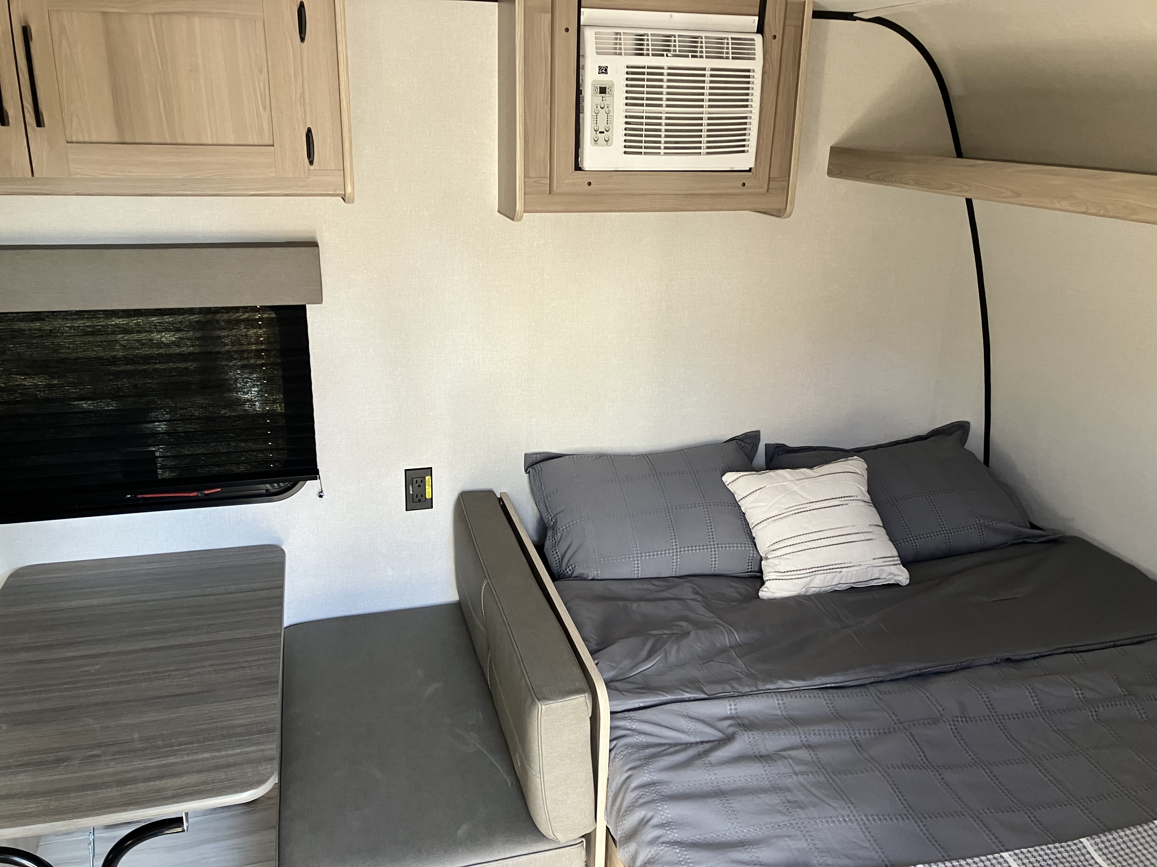 Cozy RV rental interior with bed, dinette, window, and wall-mounted AC unit, perfect for compact travel.. Coleman 17B 2025