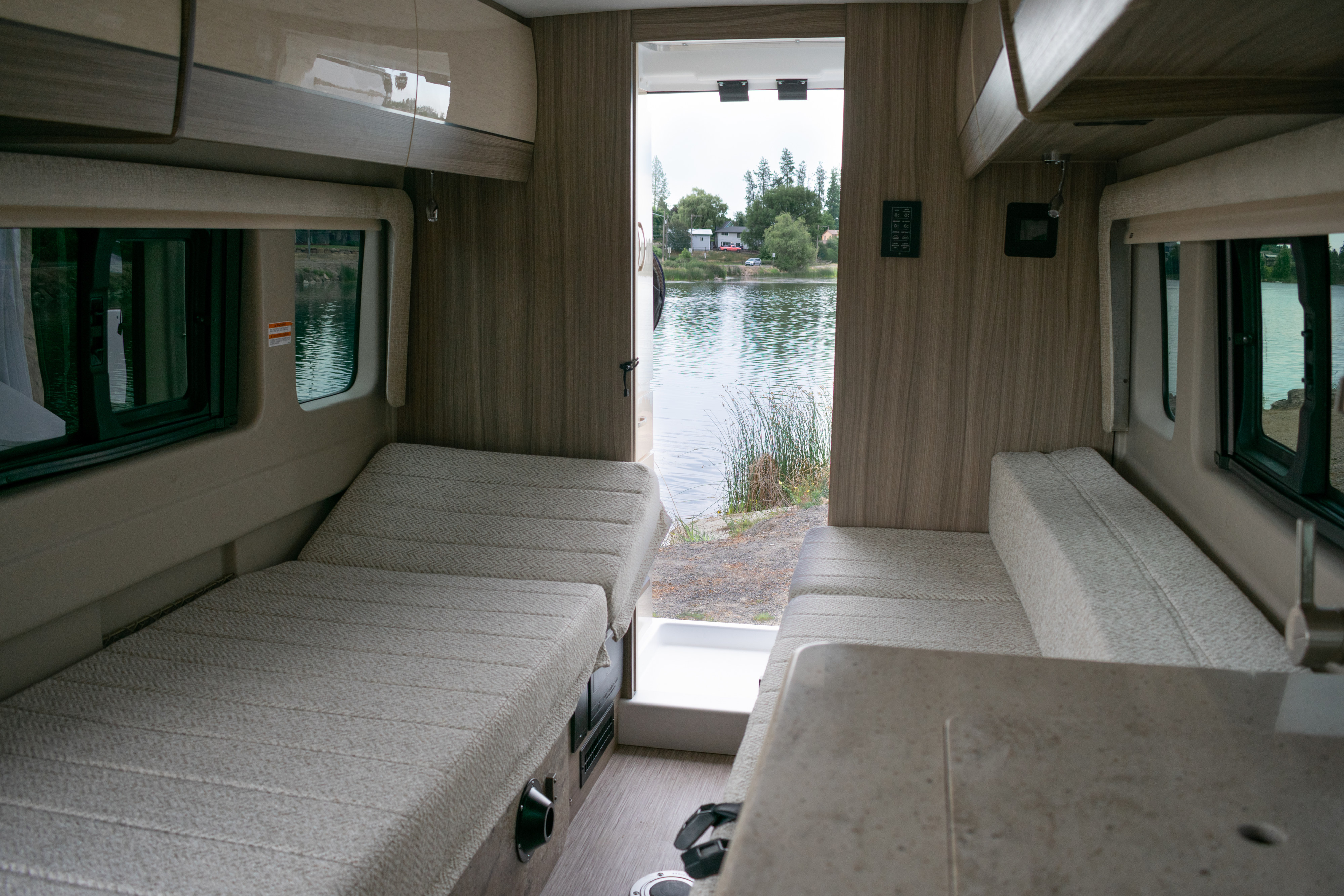 Enjoy the scenic lake view from inside this cozy RV rental, featuring comfortable bench seating and overhead storage.. Entegra Coach Ethos 2023