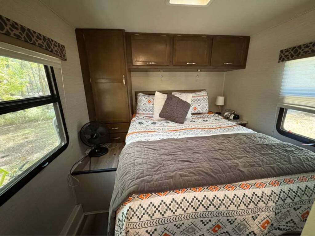 Experience a comfortable RV rental bedroom featuring a patterned bed, wood cabinets, and large windows with nature views.. Jayco 29xk 2021