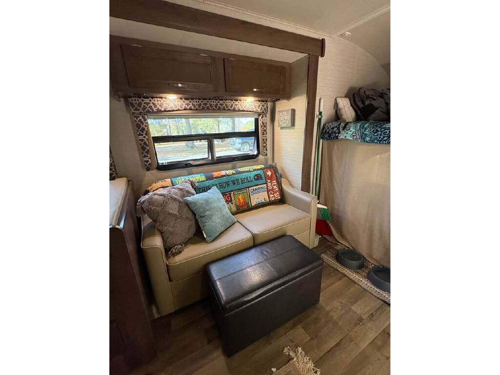 Cozy RV rental interior featuring a beige sofa, storage ottoman, and a visible bunk bed, creating a comfortable living space.. Jayco 29xk 2021