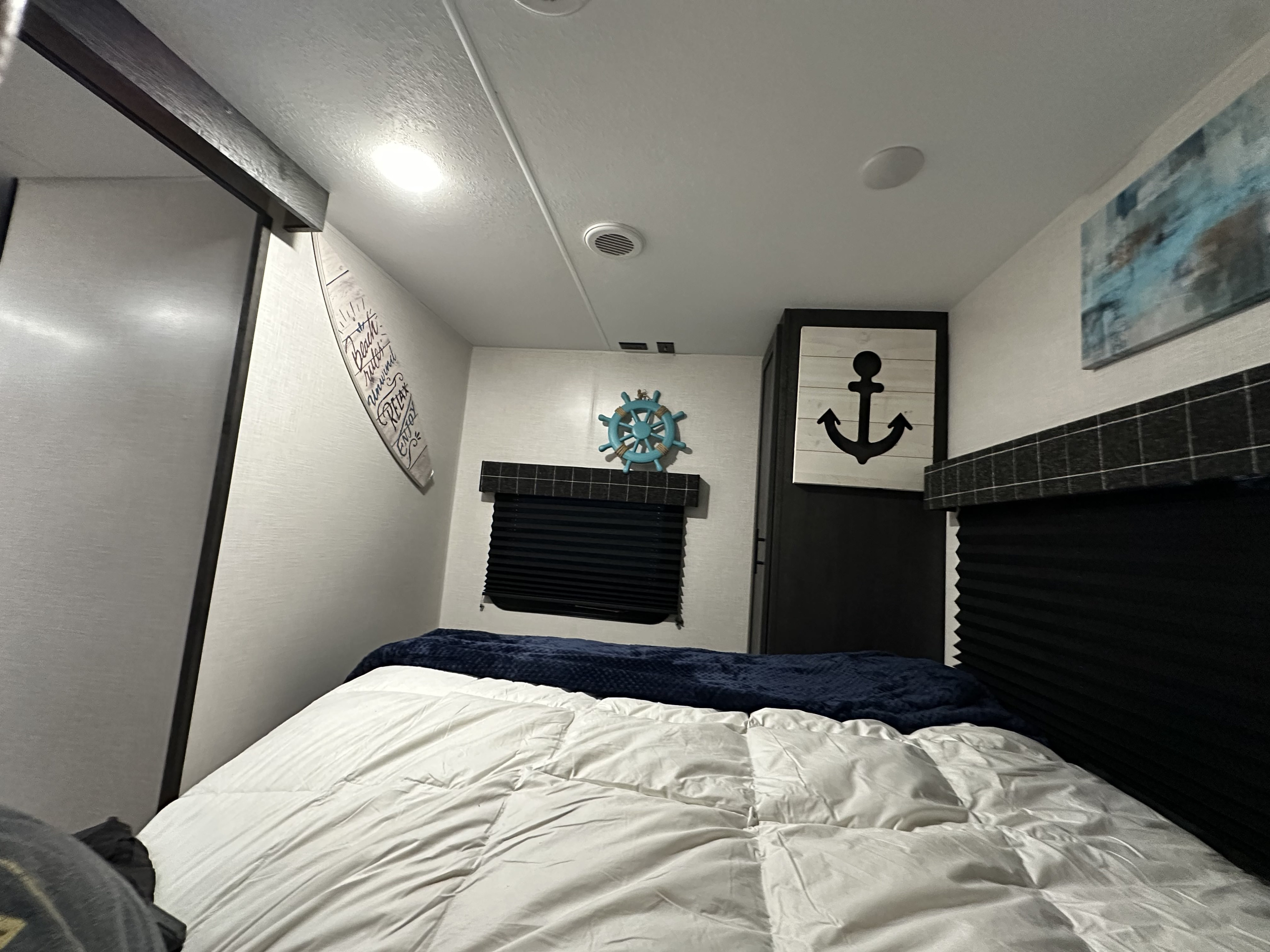 Cozy rv rental bedroom features a comfy bed, nautical decor, and dark blinds. Perfect for a restful getaway.. K-Z Manufacturing Sportsmen 2023