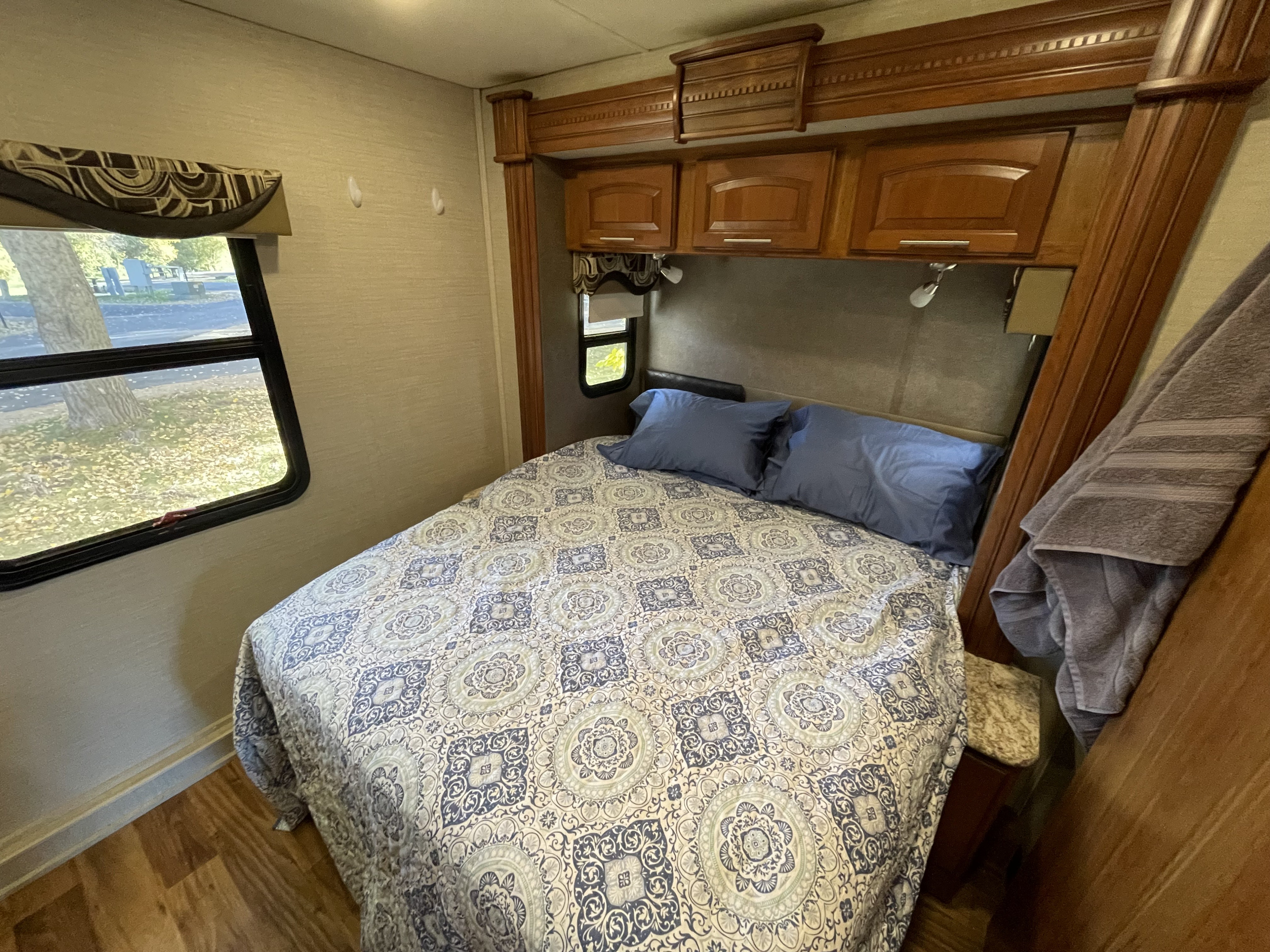 Cozy RV rental bedroom featuring a comfortable bed with patterned linens, overhead storage, and scenic window.. Jayco Precept 2017