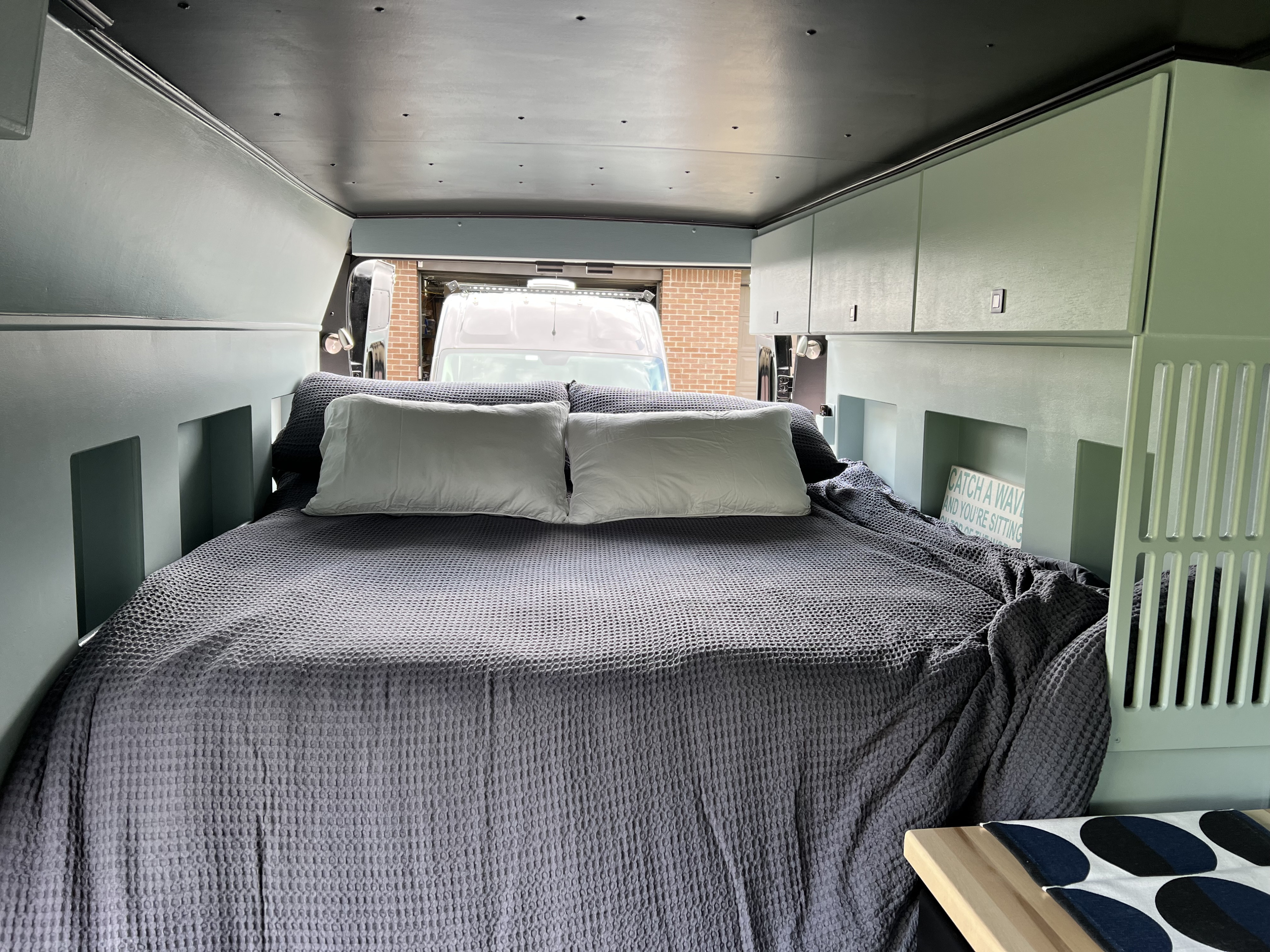Cozy RV rental sleeping area features a large bed with gray waffle-knit bedding and sage green cabinets.. Dodge RAM Promaster HR 159 WB 2022