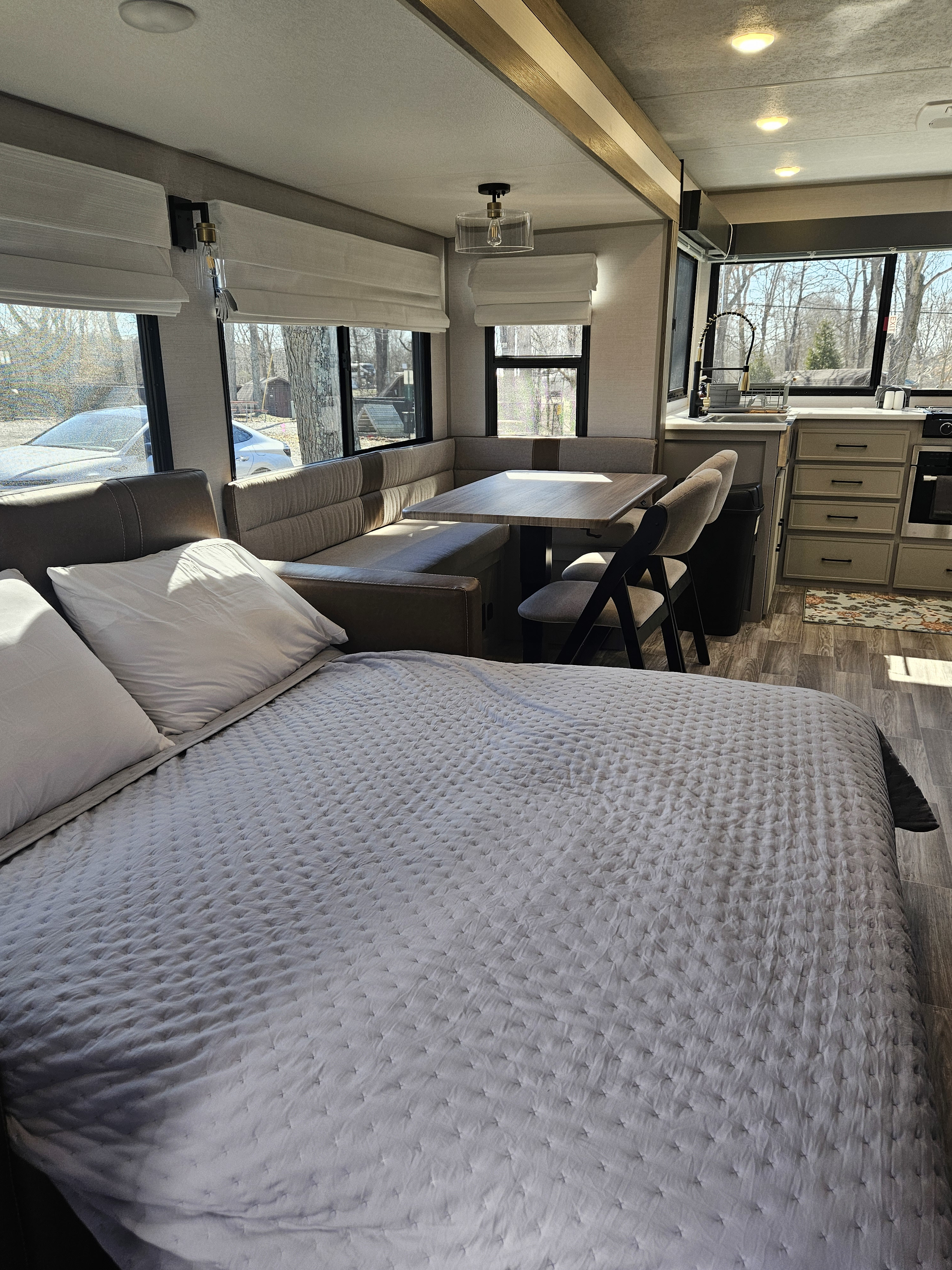 Modern RV rental interior: a pull-out bed in foreground, U-shaped dinette, and kitchen. Large windows offer a bright, cozy living space.. Forest River VIBE 3400SB 2025