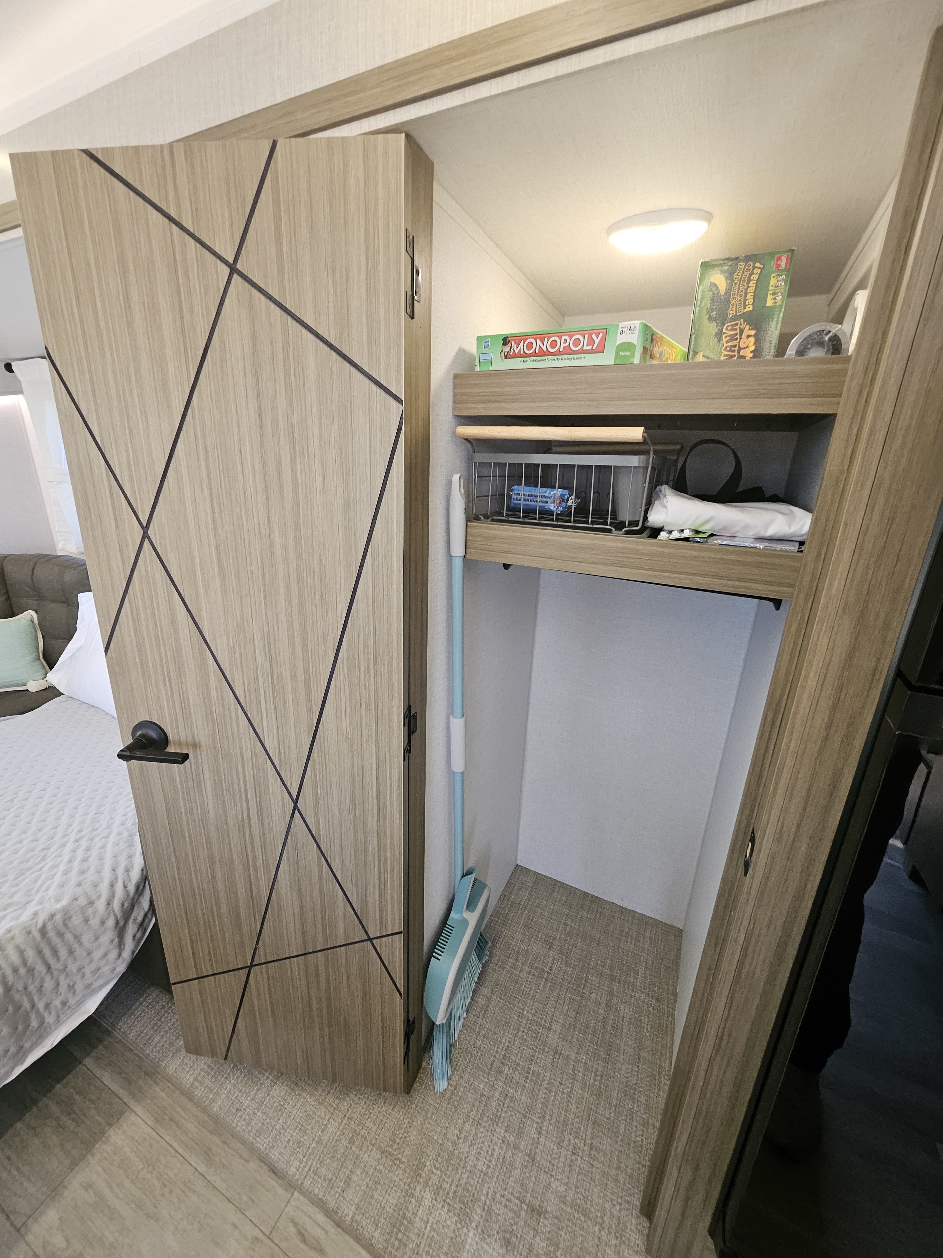 RV rental interior: Light wood closet with games shelf, pull-out basket, and broom offers clever storage.. Forest River Wildwood 34Veranda 2025