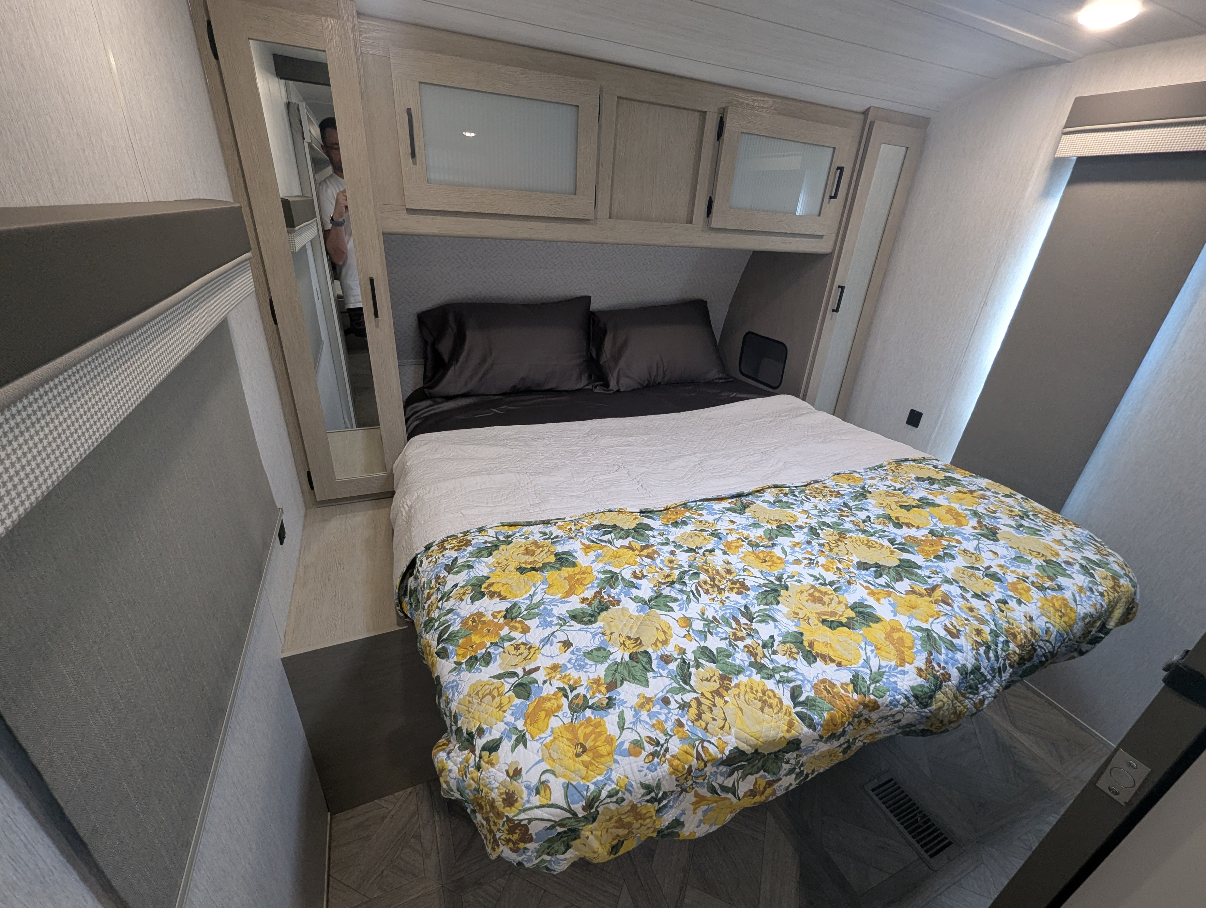 RV rental bedroom with a bright floral comforter, dark bedding, wooden overhead cabinets, and mirrored closet doors.. Forest River Wildwood 2023