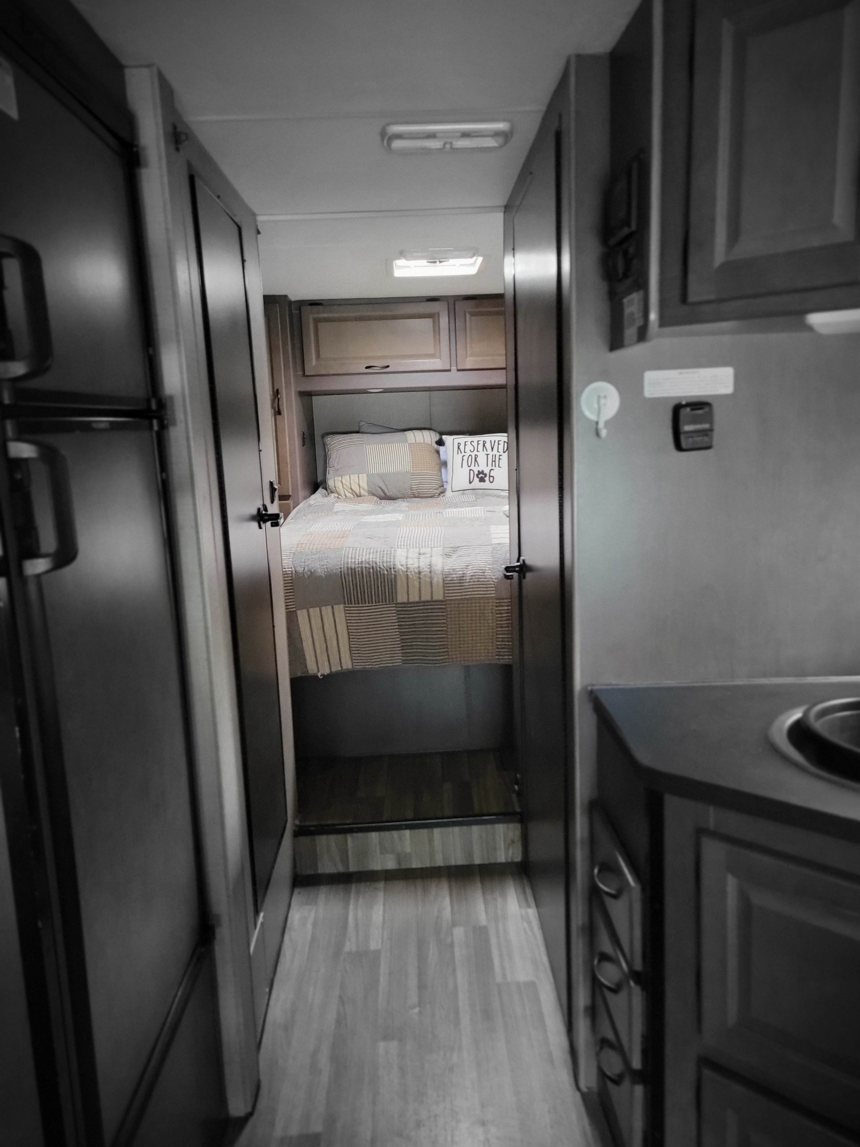 View into an RV rental interior: hallway leading to a cozy bedroom with a patterned bed & "reserved for the dog" pillow.. Thor Majestic 2019