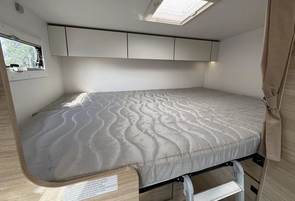 Modern RV rental sleeping area: a large bed under overhead cabinets, with a window, skylight, and access ladder.. Challenger C194 START EDITION 2025