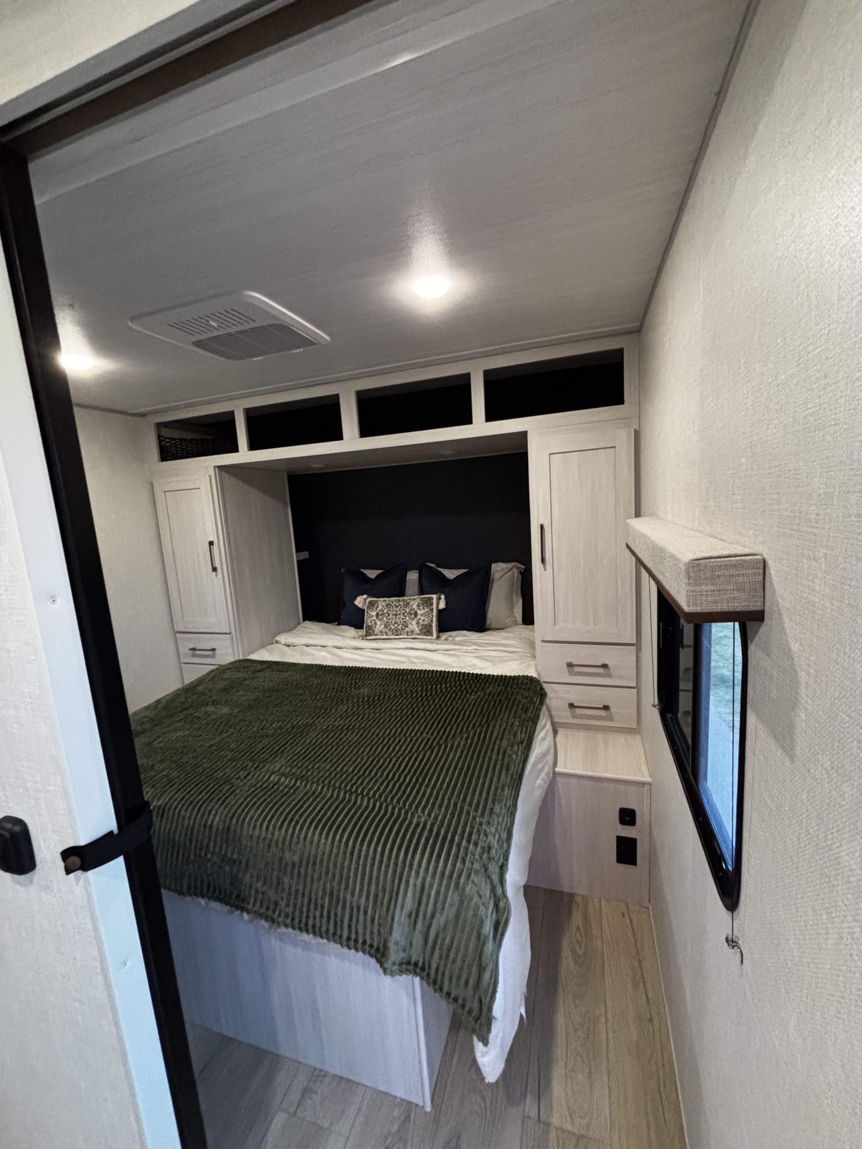 Cozy modern RV rental bedroom interior with comfortable bed, overhead storage, and window. Ideal for travel adventures.. Forest River Surveyor 27 Camp 2025