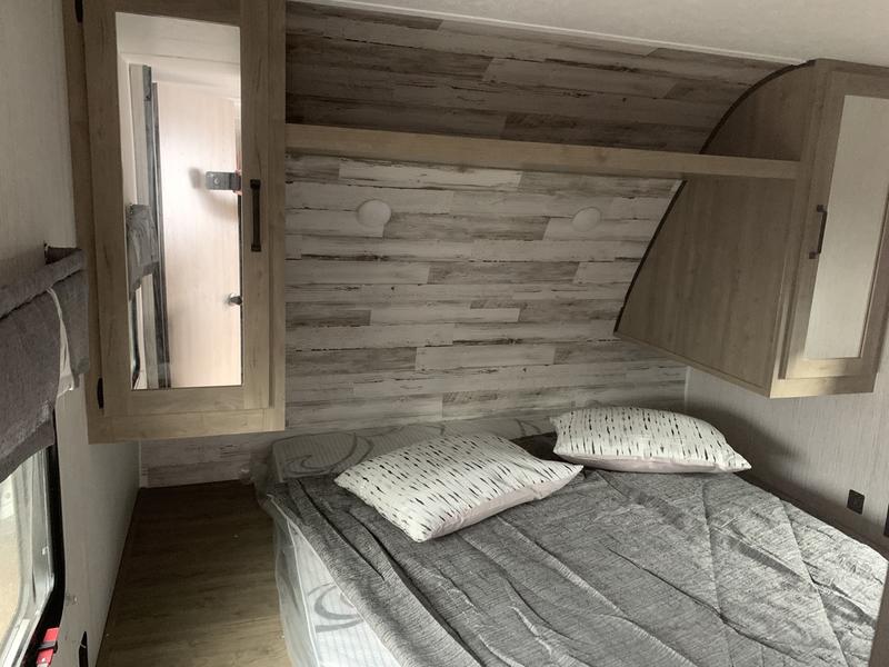 Modern RV rental bedroom featuring a bed, wood-look walls, and overhead storage. Ideal for comfortable travel.. Forest River Puma 2022