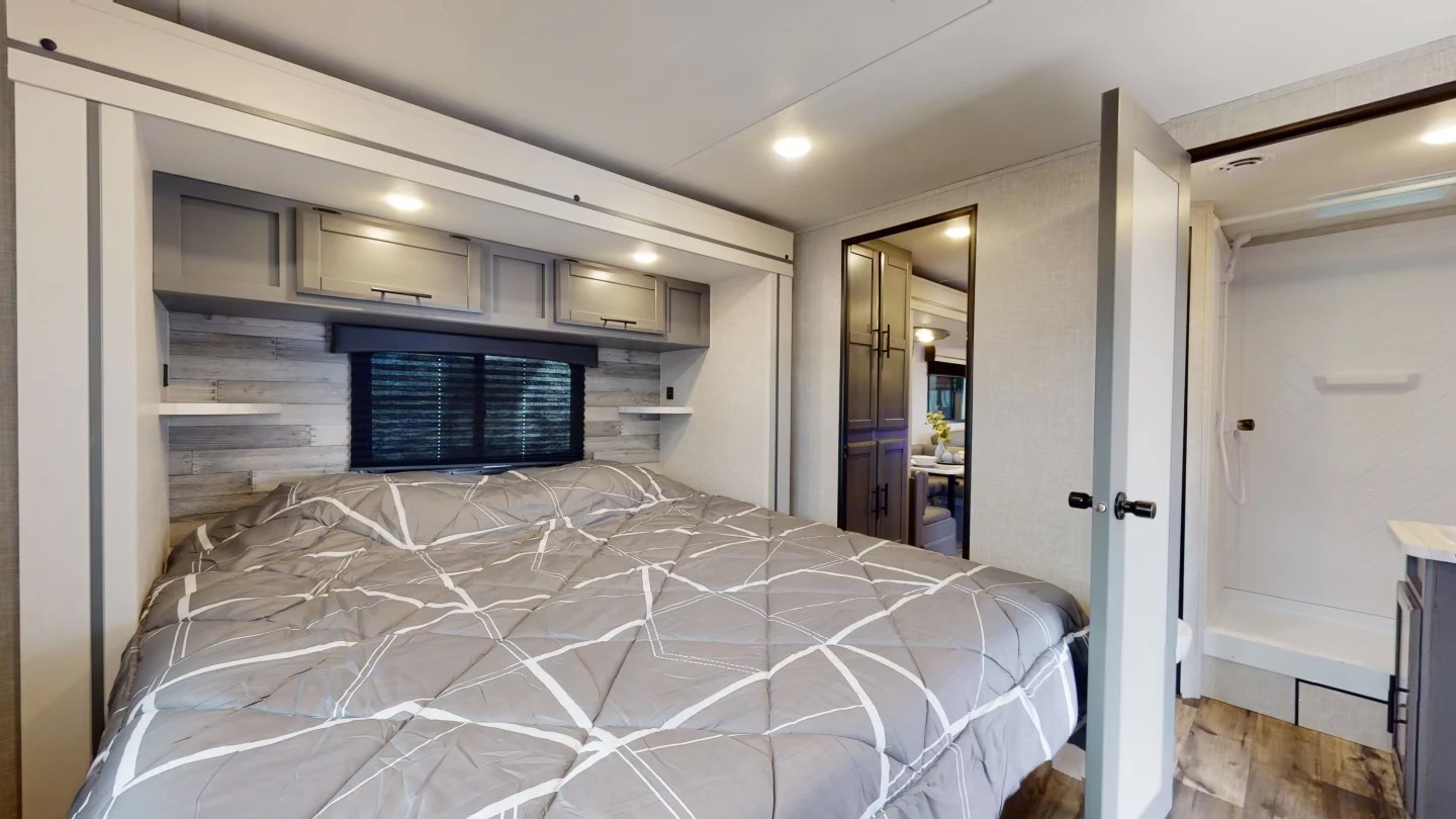 Cozy RV rental bedroom features a gray bed, ample overhead storage, and convenient access to the private bathroom.. Crossroads Zinger 2025