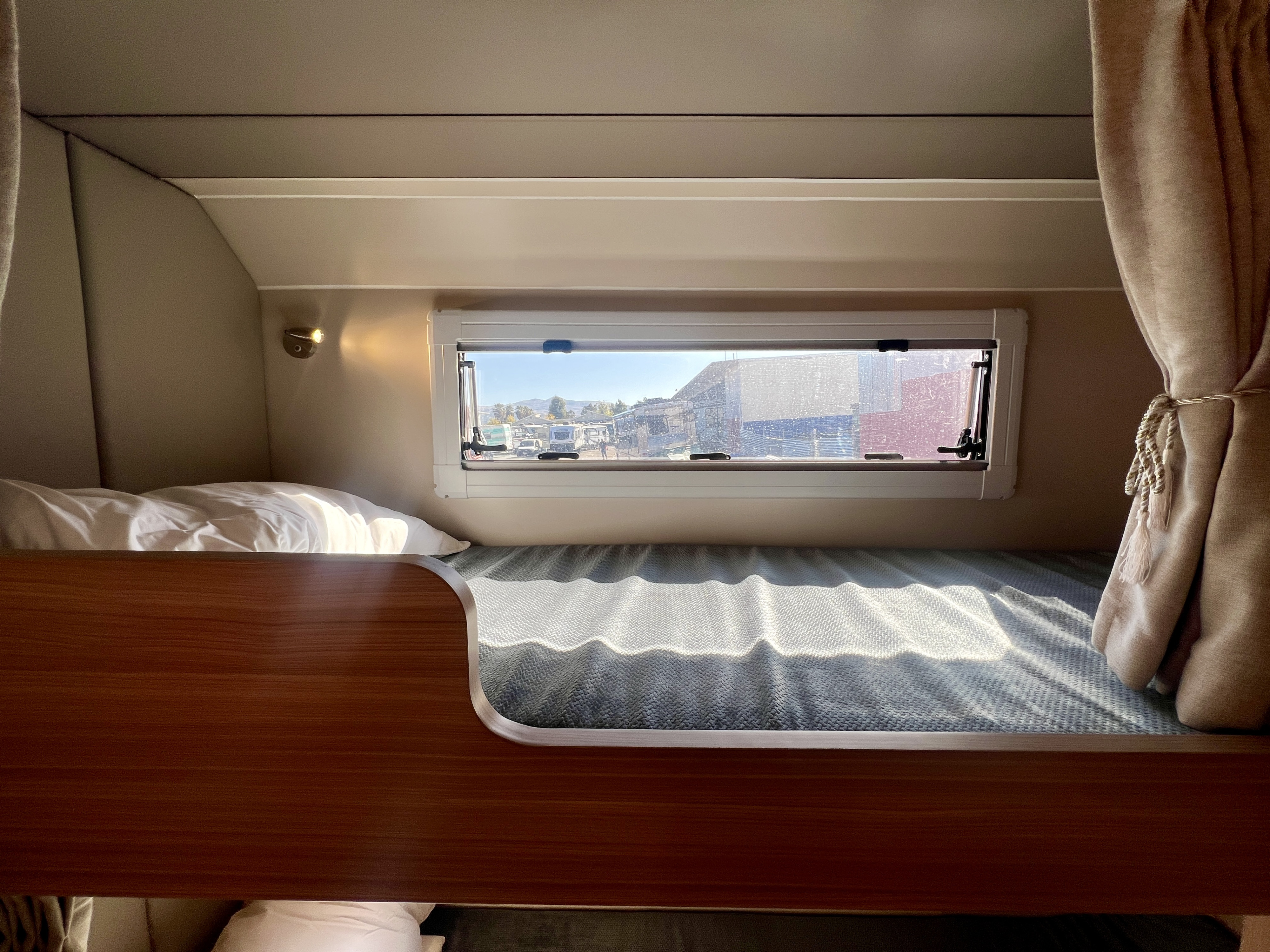 Cozy bunk bed inside an RV rental, offering a bright window view of other campers and mountains.. Black Series HQ17 2025