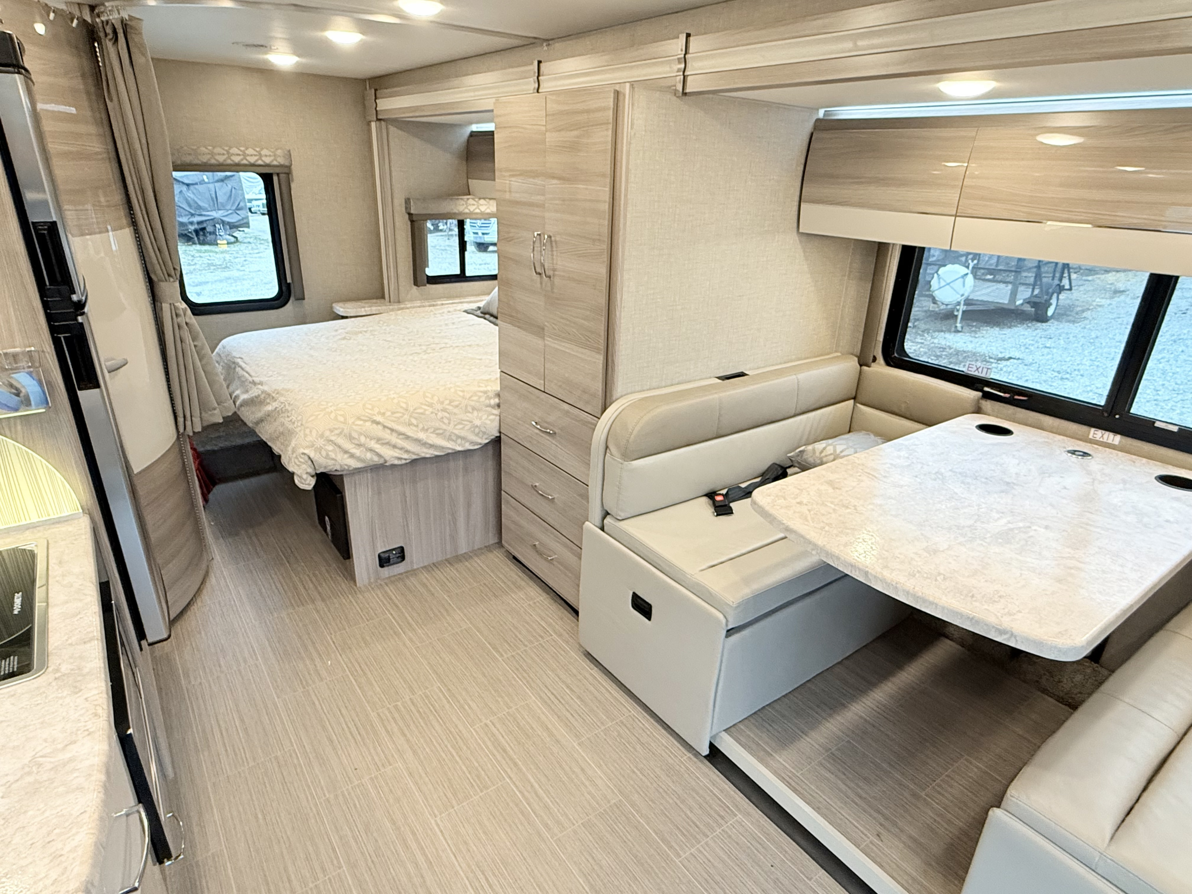 Bright rv rental interior showing a comfortable bed, dinette, and sleek kitchen. Light tones and modern design enhance travel.. Thor Delano 2023