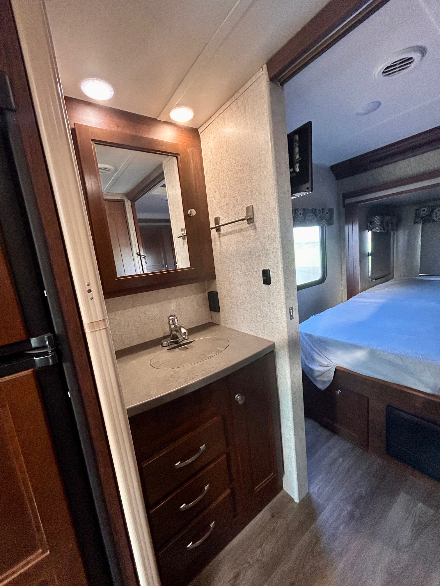 RV rental interior: a compact bathroom vanity with sink, mirror, and adjacent cozy bedroom with a bed. Ideal for travel adventures.. Forest River Sunseeker 2017