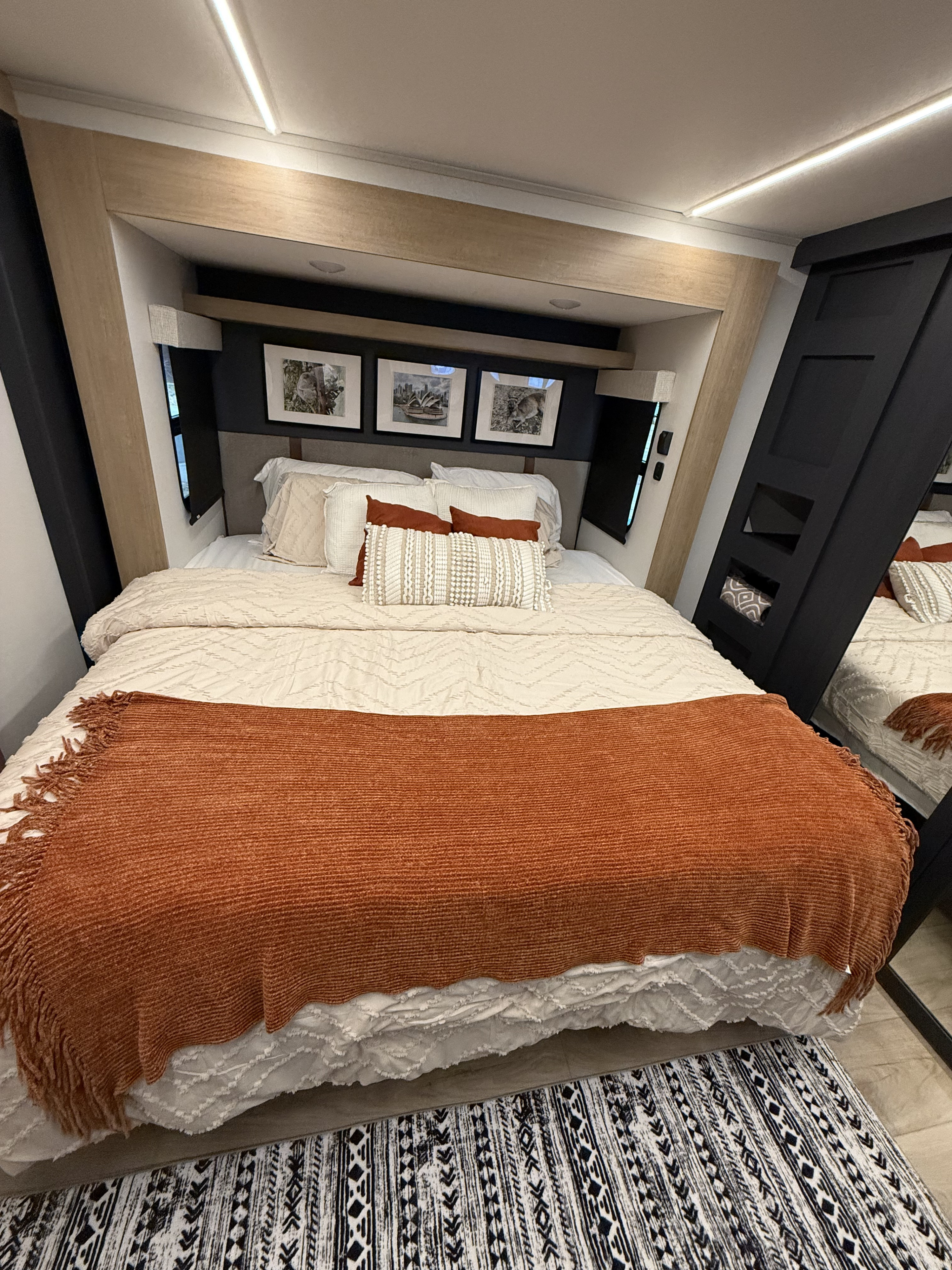 Relaxing RV rental bedroom showcasing a neutral bed, rust throw, framed art, and built-in storage.. Heartland Cyclone 2025
