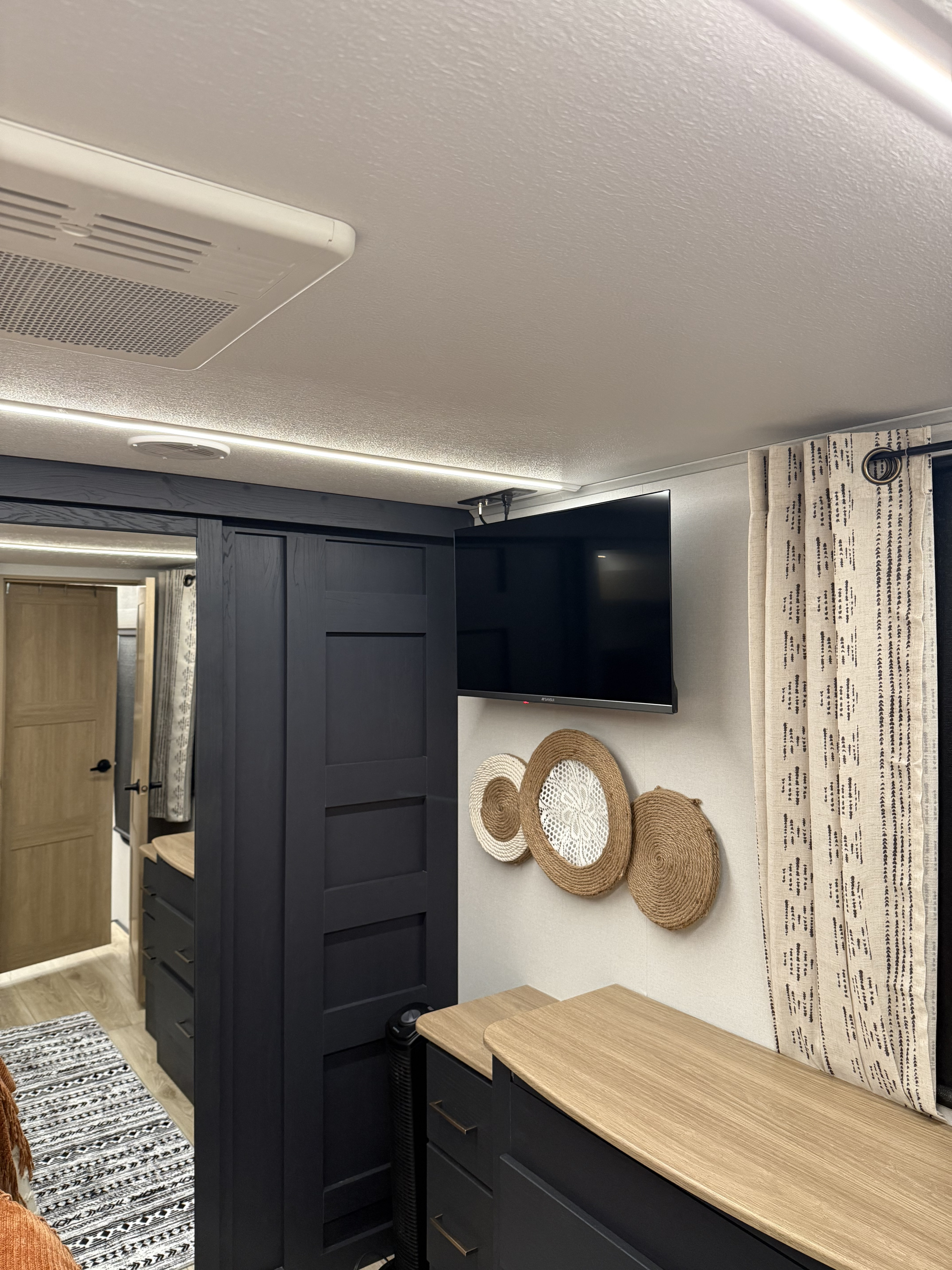 RV rental: Brightly lit interior bedroom with TV, sleek black storage, light wood counters & decorative wall art.. Heartland Cyclone 2025