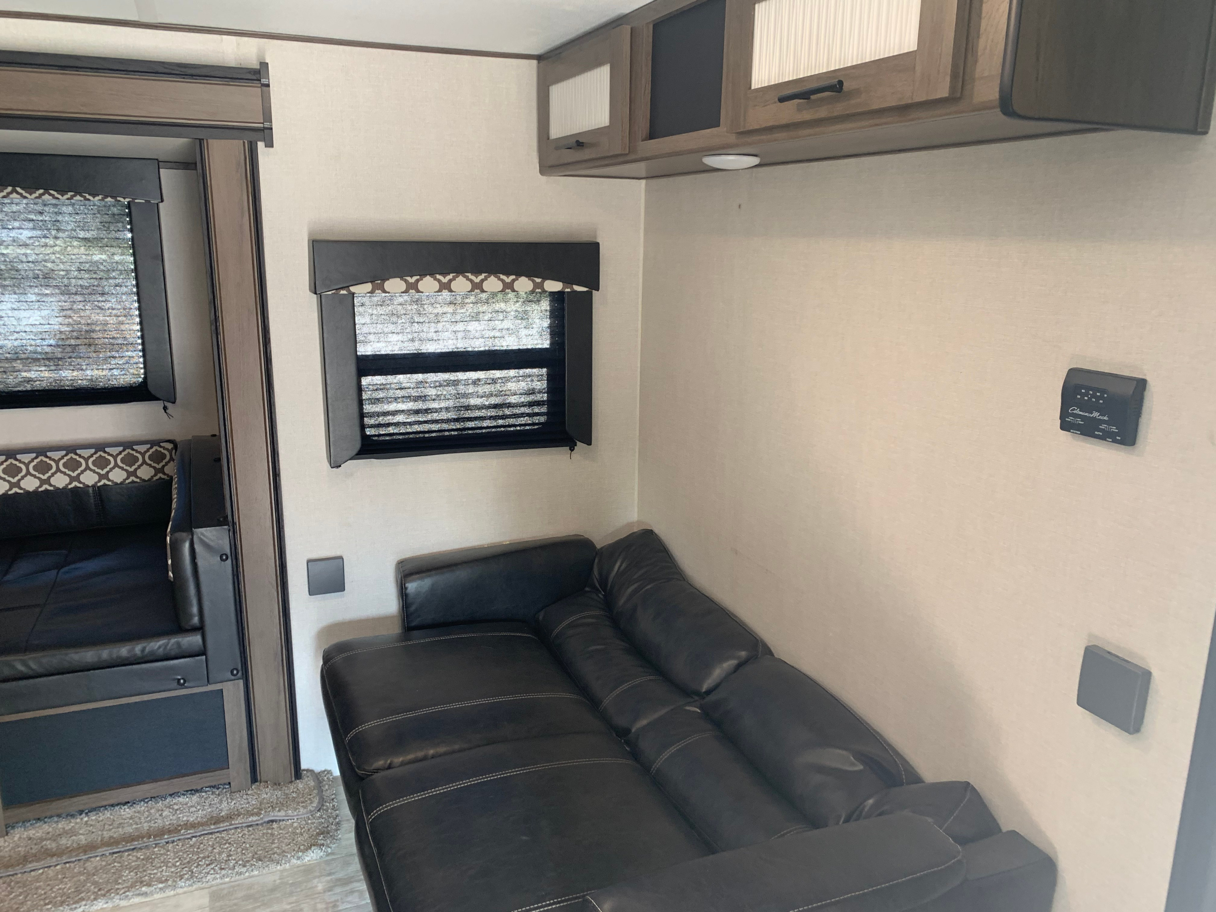 Inside an RV rental: view of a comfy black leather sofa, dinette with patterned cushions, overhead cabinets, and window.. Prime Time RV Avenger 2021