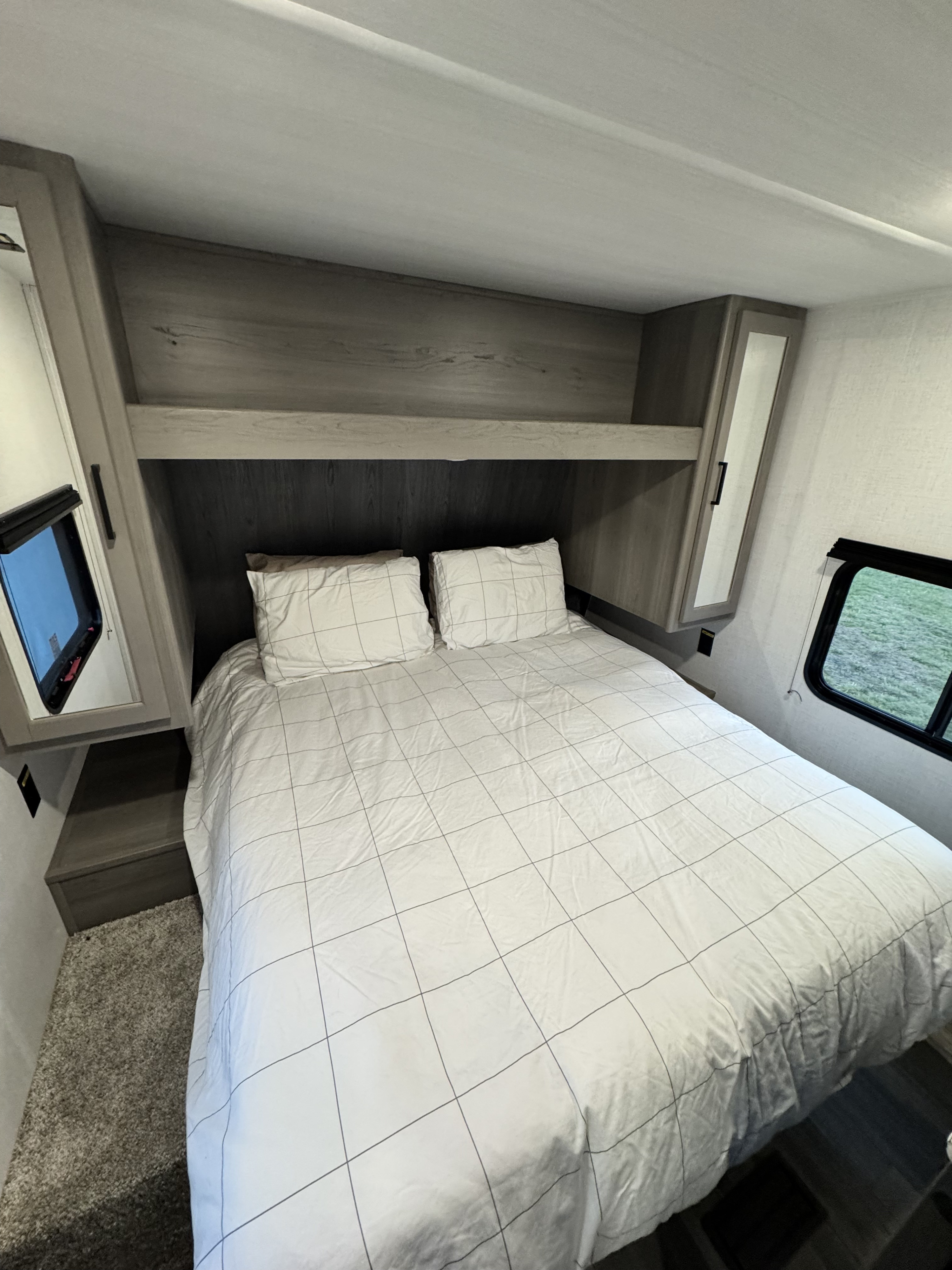 Compact RV rental bedroom interior with grid bedding, built-in storage, and windows for travel.. Keystone RV Hideout 2024