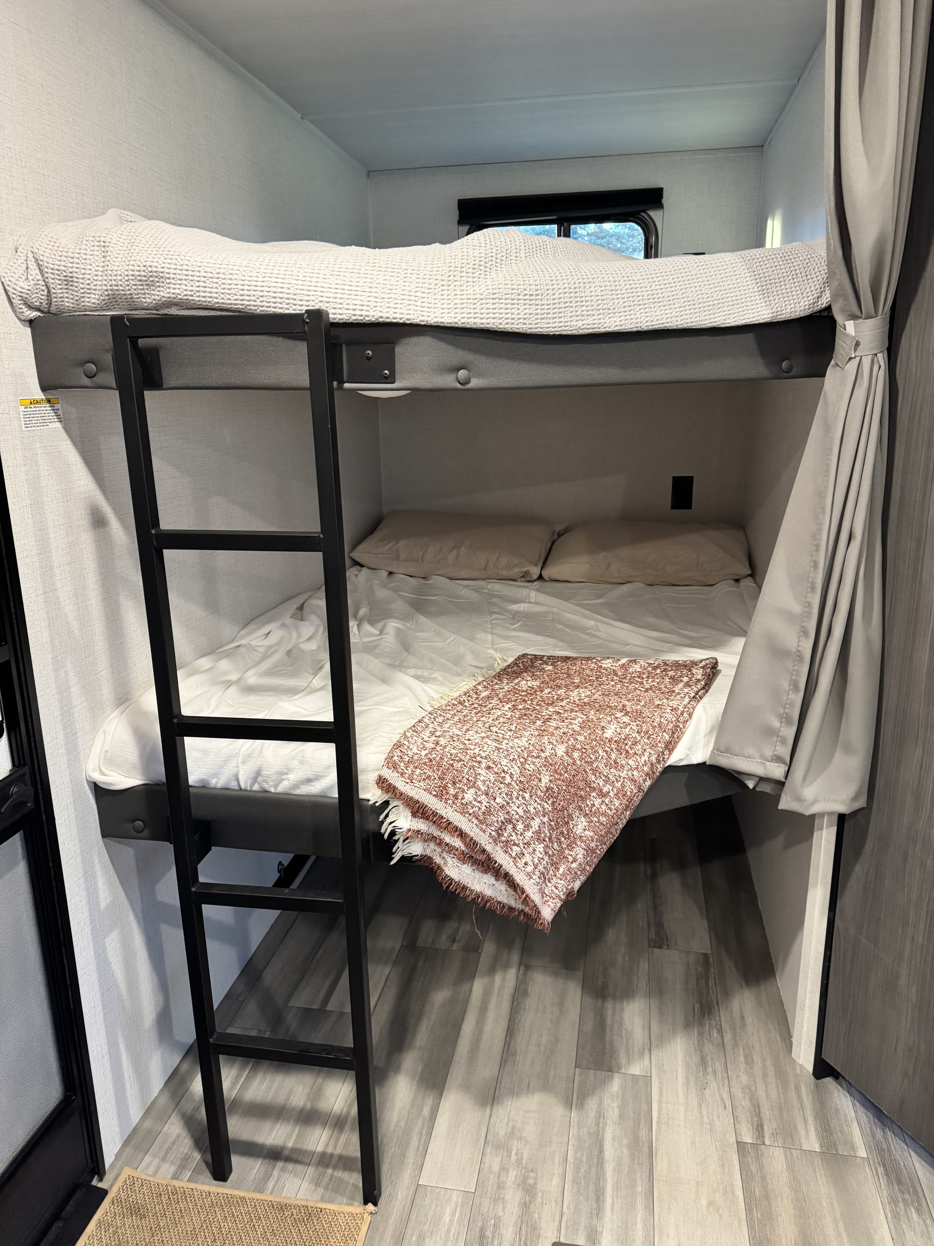 RV rental bunk beds: a cozy interior sleeping area with ladder, blankets, pillows, and a window.. Keystone RV Hideout 2024