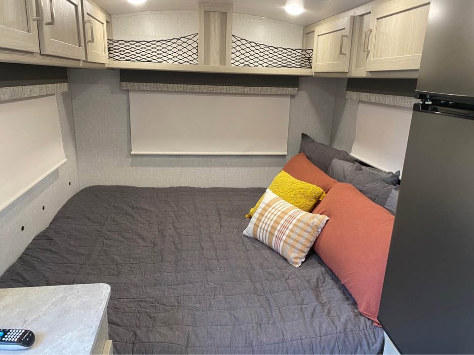 Inviting RV rental bedroom: bed with grey comforter & colorful pillows, overhead cabinets, and window blinds.. Forest River Flagstaff E-Pro 2022