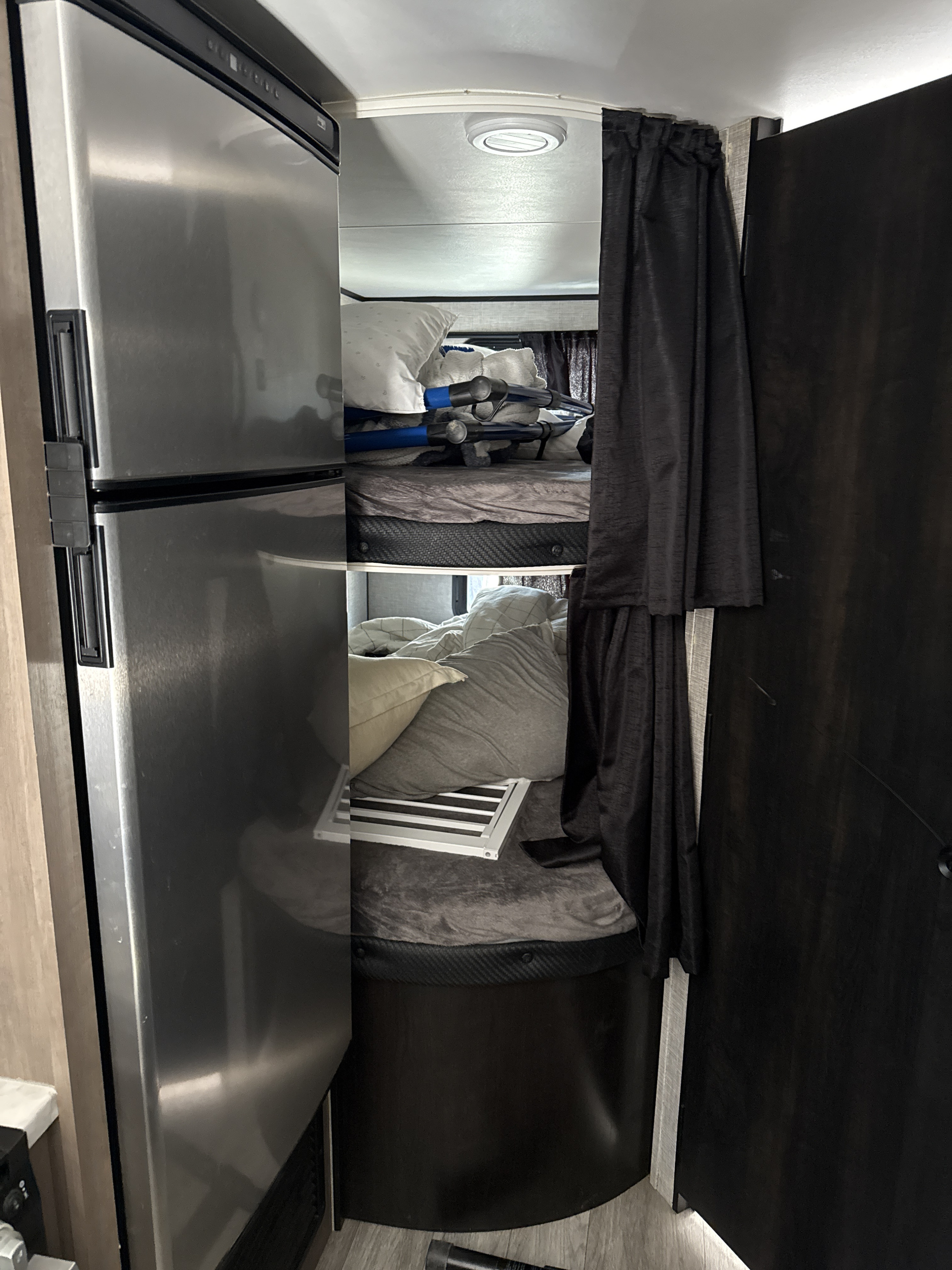 RV rental interior featuring bunk beds with pillows, dark curtains, and a stainless steel refrigerator.. Jayco Jay Flight 2023