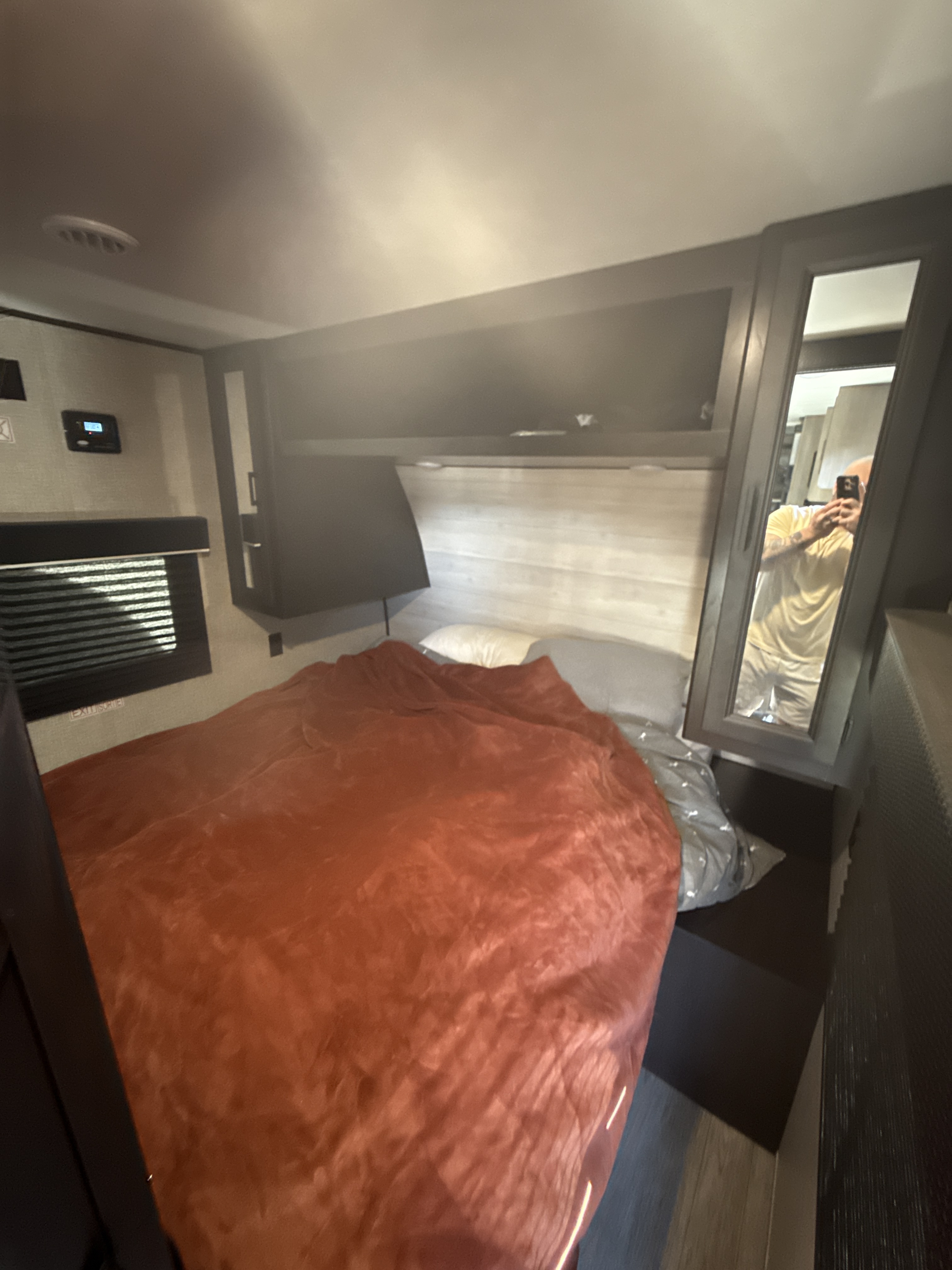 Inside a compact RV rental bedroom with a large bed, mirrored closet, overhead storage, and control panel.. Jayco Jay Flight 2023