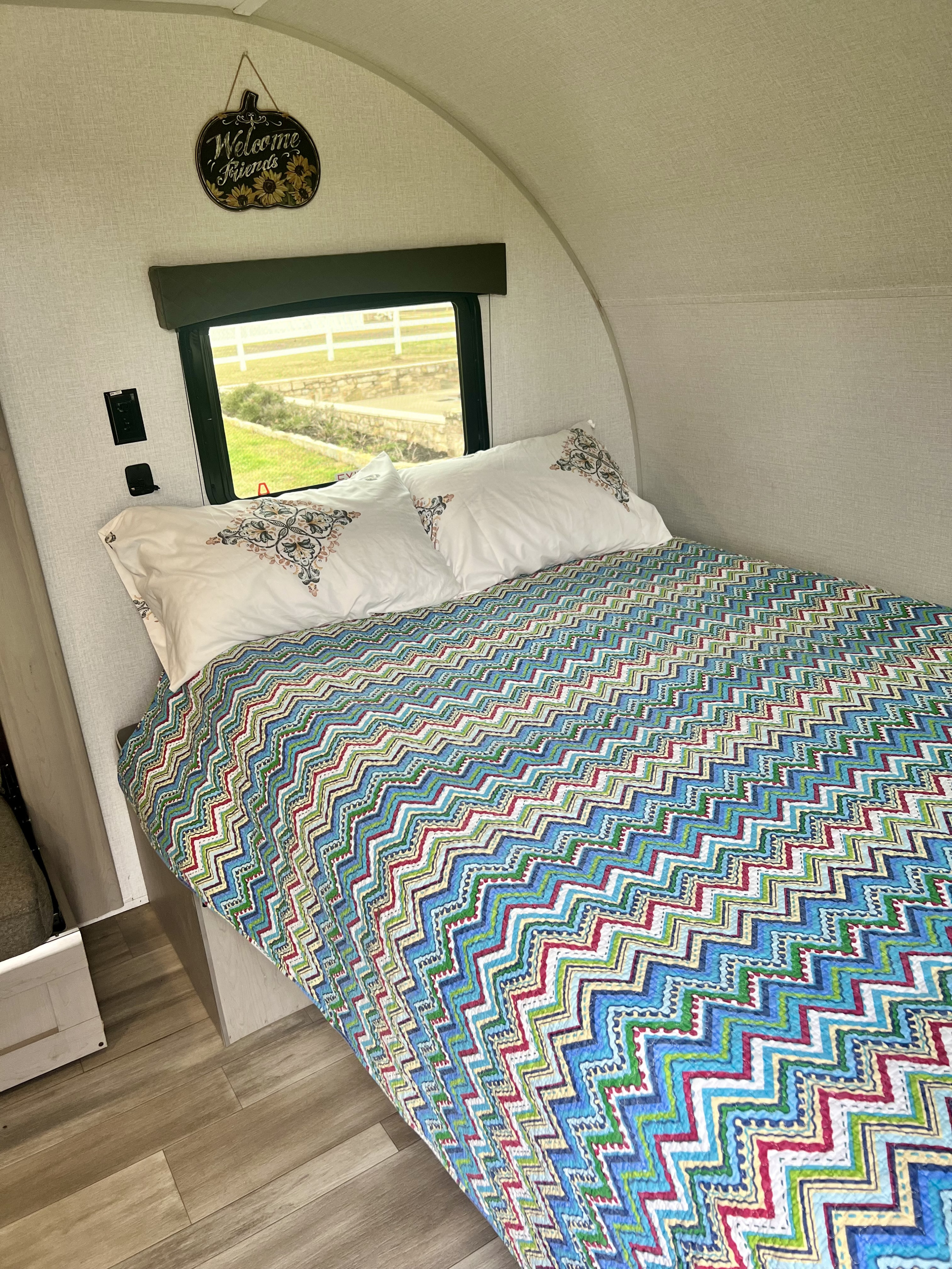 Cozy RV rental bedroom featuring a vibrant zigzag quilt, white pillows, and a scenic window view outside.. Forest River Viking 3K 2024