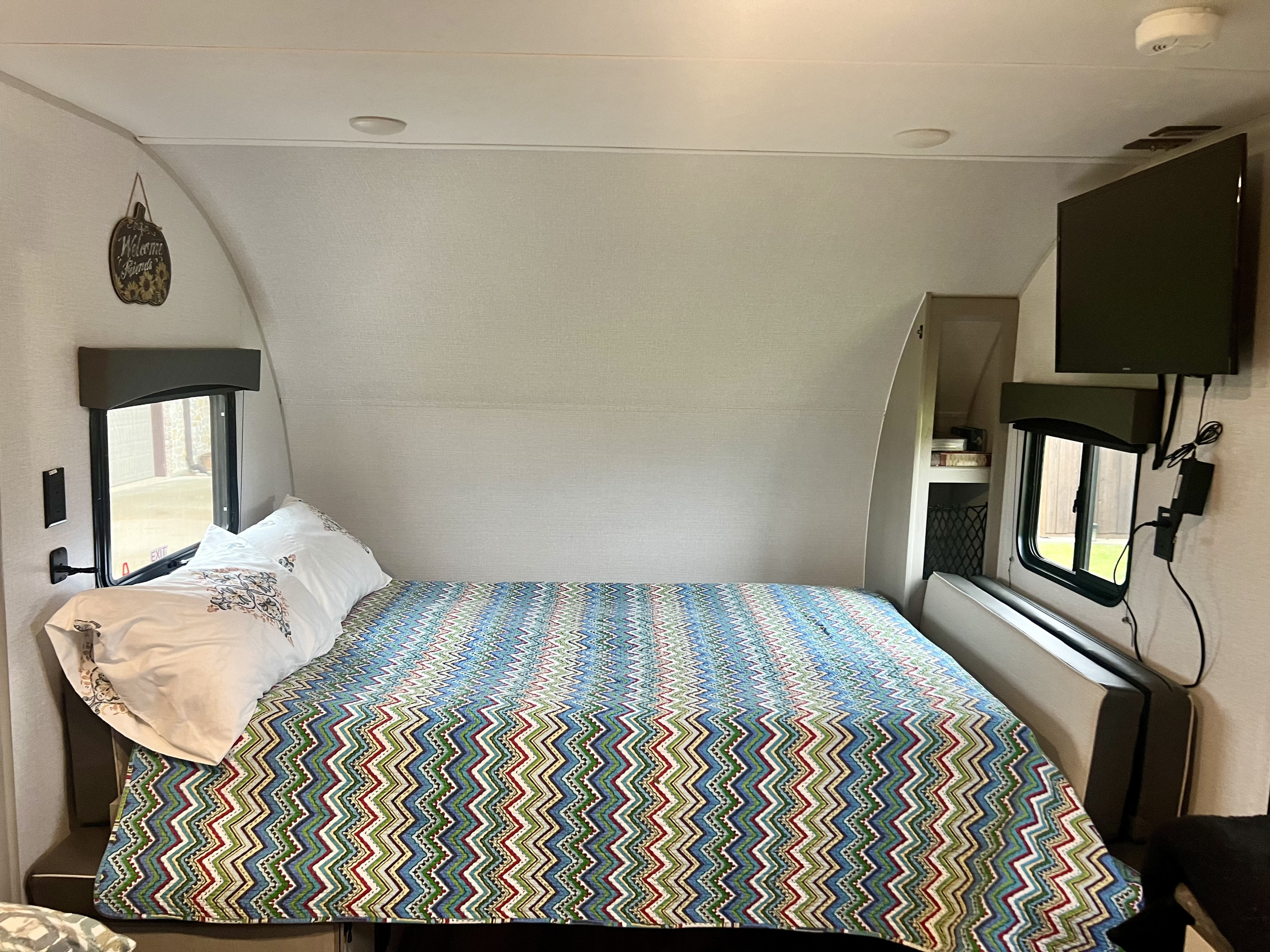 RV rental bed area featuring a colorful zig-zag quilt, windows, and a mounted TV, perfect for compact living.. Forest River Viking 3K 2024