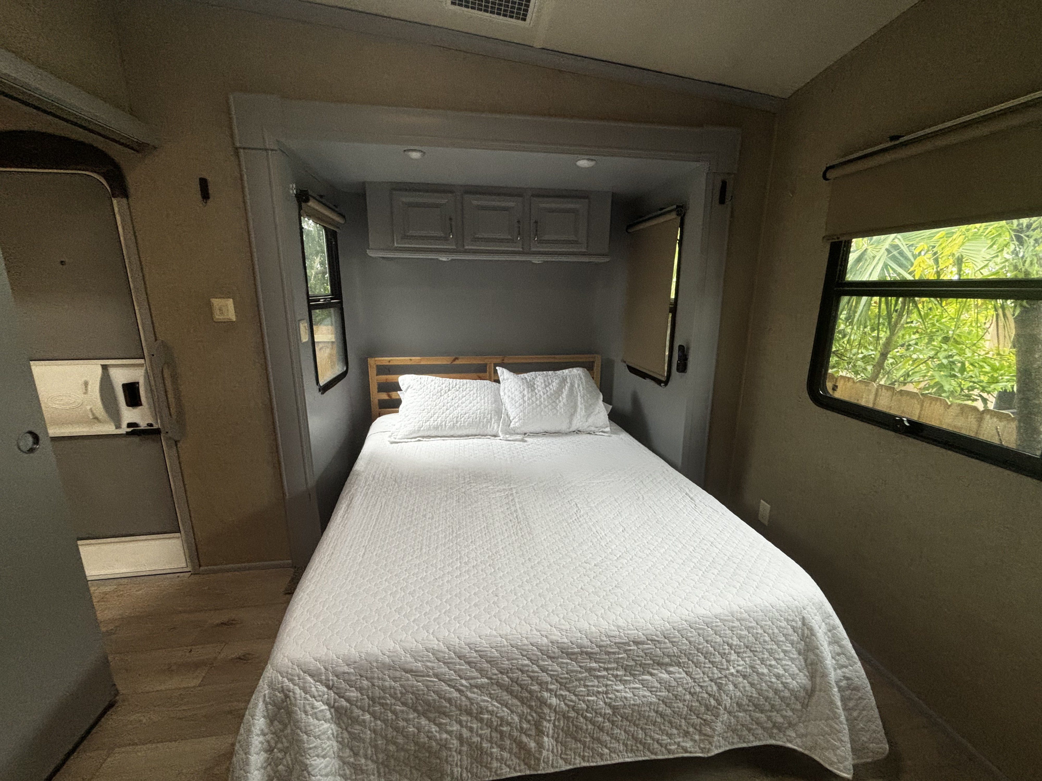 Cozy RV rental bedroom featuring a comfortable bed, overhead cabinets, and windows with scenic views.. Cedar Creek Hathaway 2016
