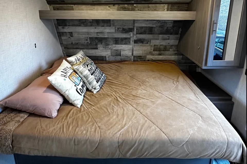 Cozy RV rental bedroom with a comfortable bed, rustic wood accent wall, and built-in storage.. Keystone RV CM18BH22 2022