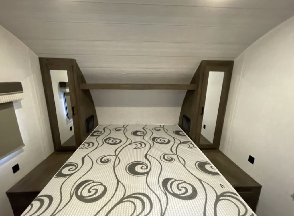 Inside an RV rental bedroom: a bed with patterned mattress, surrounding storage cabinets, and an overhead shelf.. Forest River Salem Cruise Lite 2022