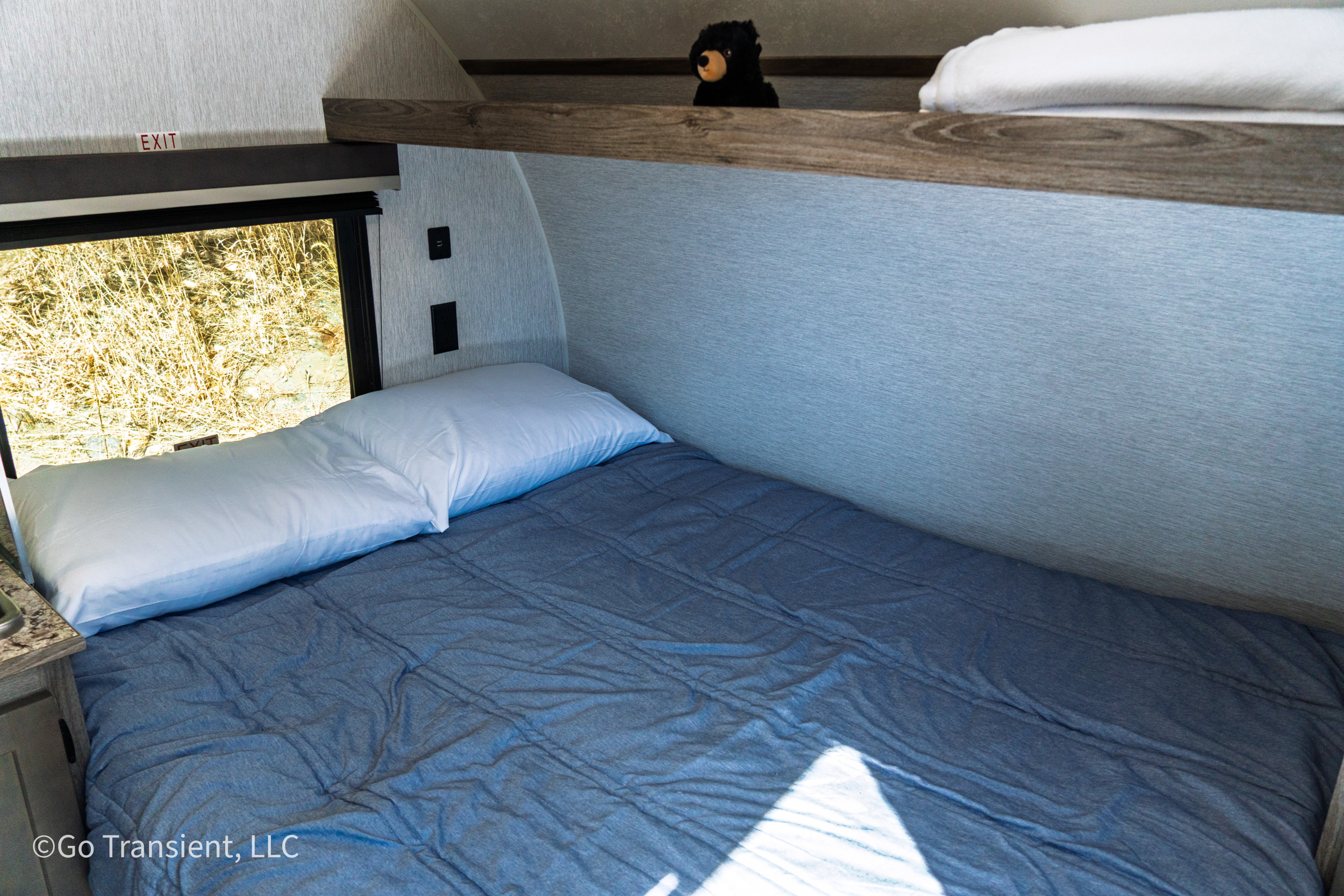 RV rental: Cozy bunk bed with white pillow & blue comforter. Window shows golden grass, upper bunk has a bear plush.. Sunset Park RV Sun Lite LTD 13BH 2025