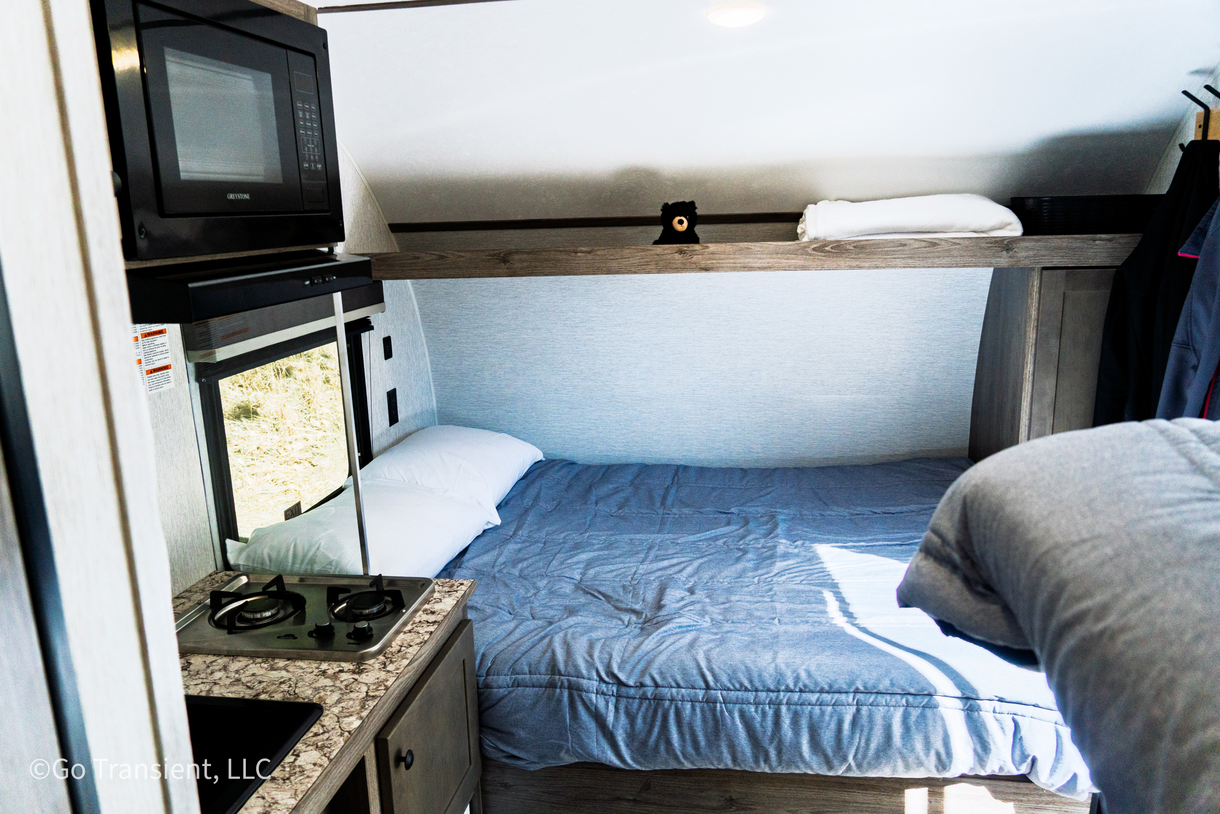 Inside this RV rental: a compact living area with bed, microwave, and stove for your travel comfort.. Sunset Park RV Sun Lite LTD 13BH 2025