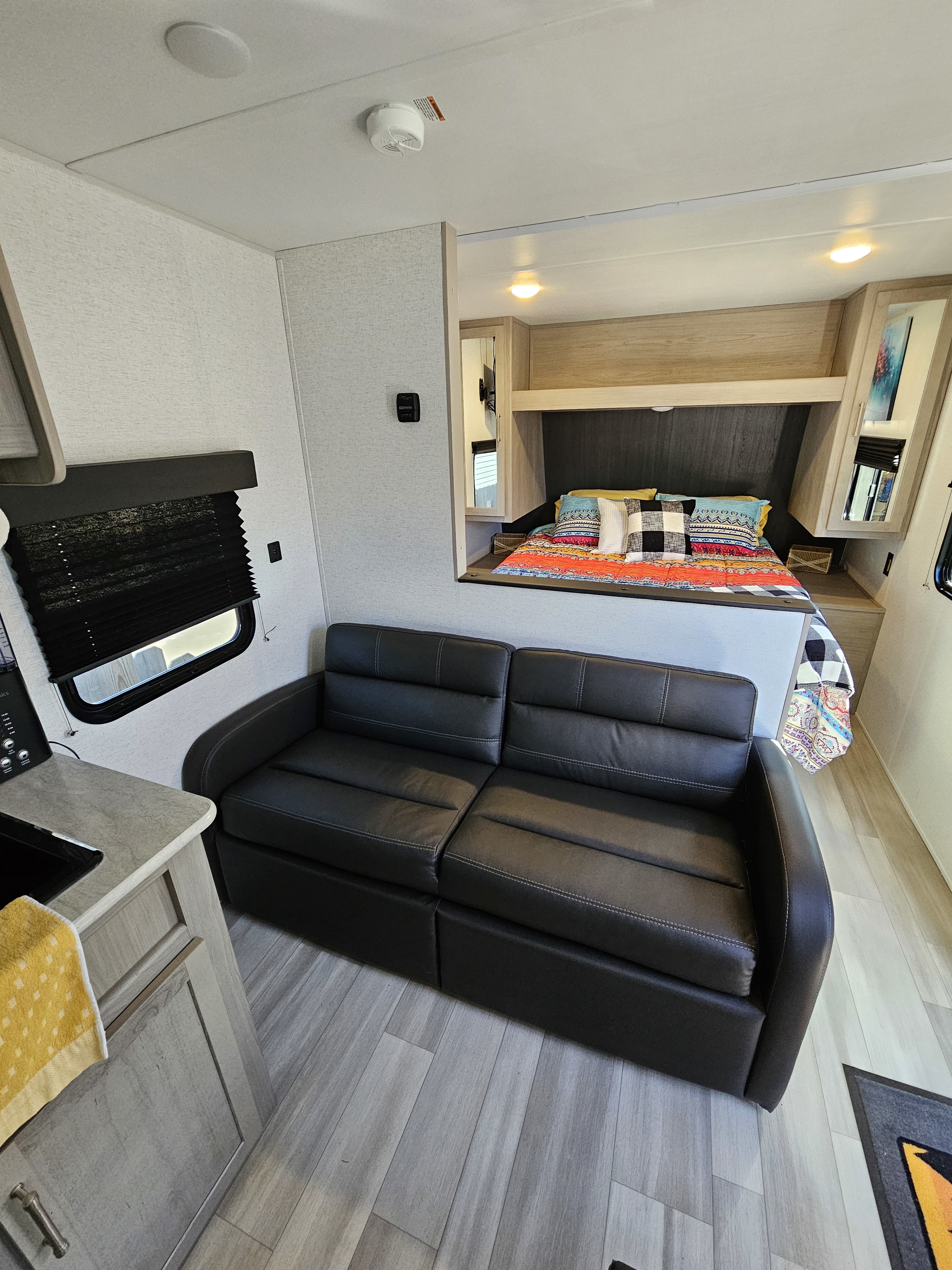 Modern RV rental: black sofa in living area, kitchen counter left, bed with colorful bedding in bedroom.. Keystone 260 bhs 2024