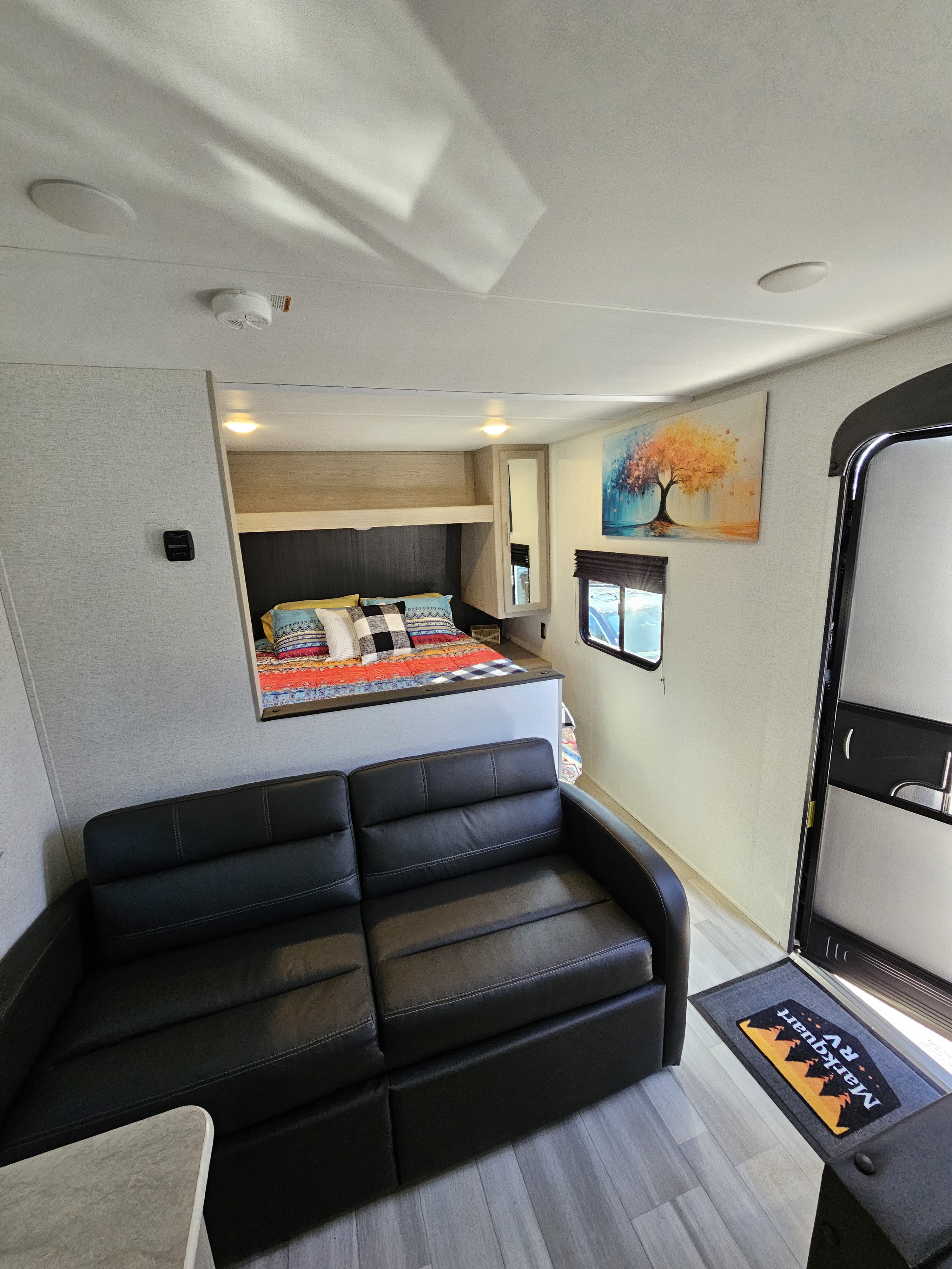 Inside a spacious Markquart RV rental: cozy bed with colorful bedding, black sofa, and main door with welcome mat.. Keystone 260 bhs 2024
