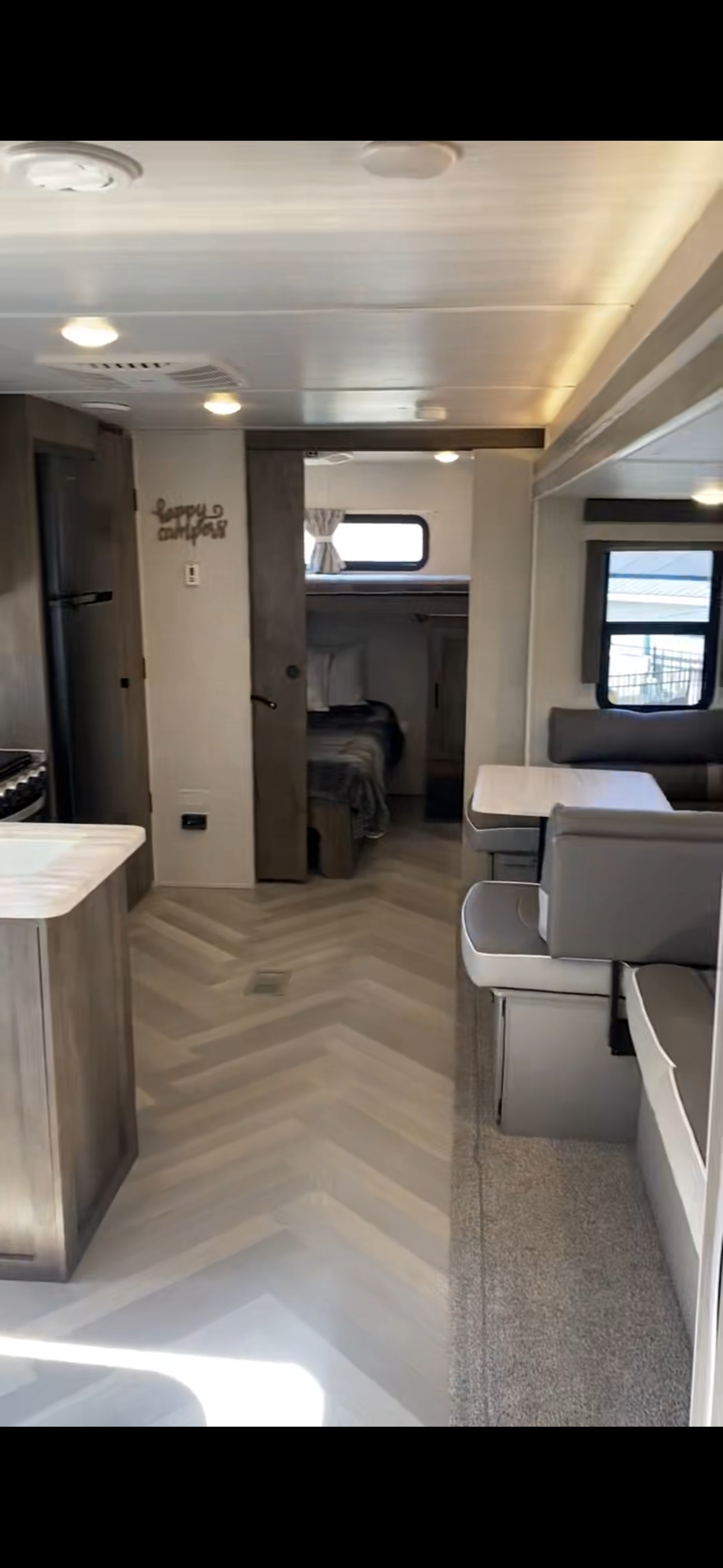 Bright RV rental interior: modern kitchen, herringbone floor, dinette, and bunk room. Ready for adventure.. Forest River Wildwood 2021