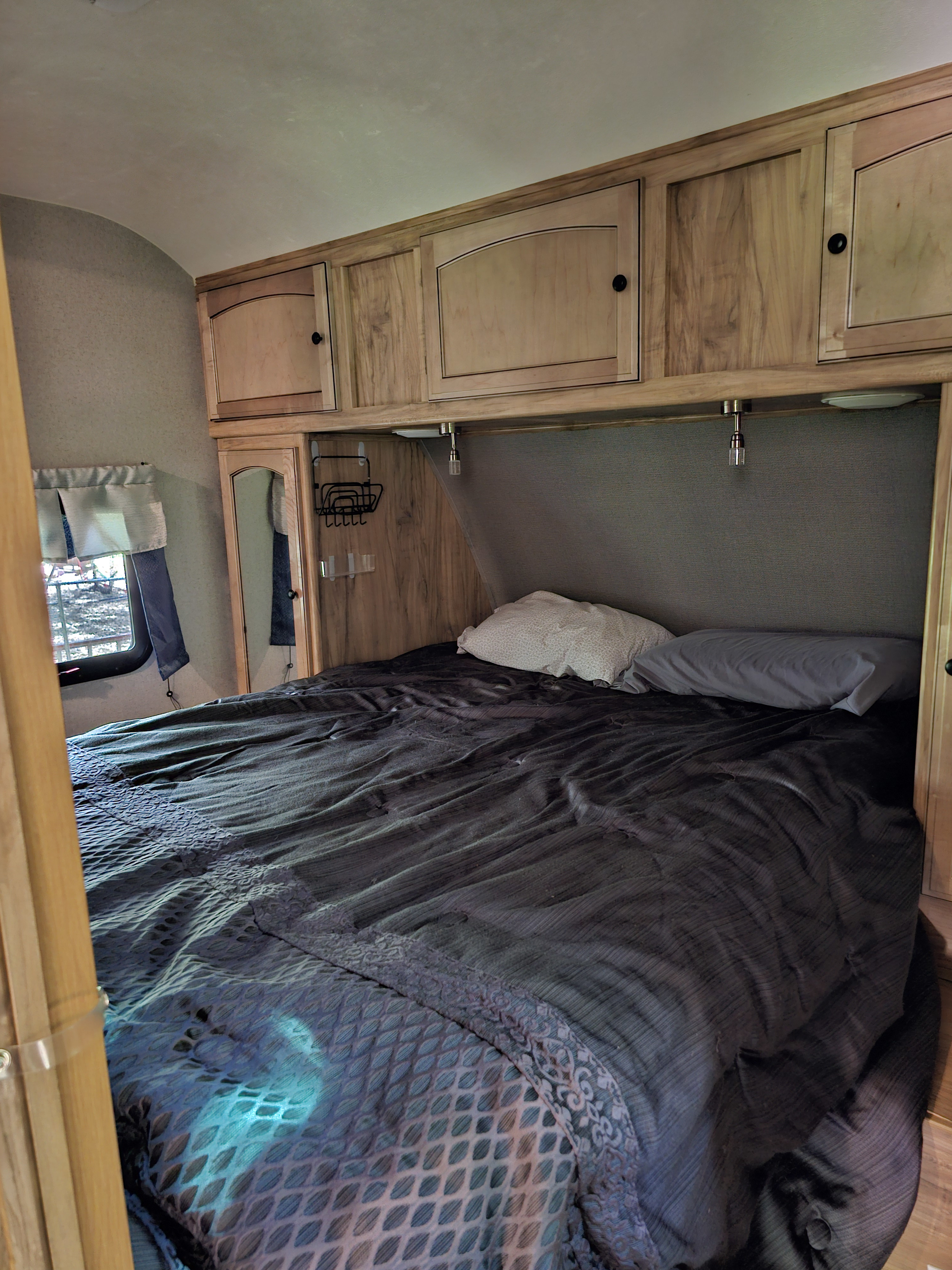 Inside an RV rental, a cozy bedroom with a comfortable bed, wood cabinets, and window view.. Coachmen Freedom Ultralite Express 2018