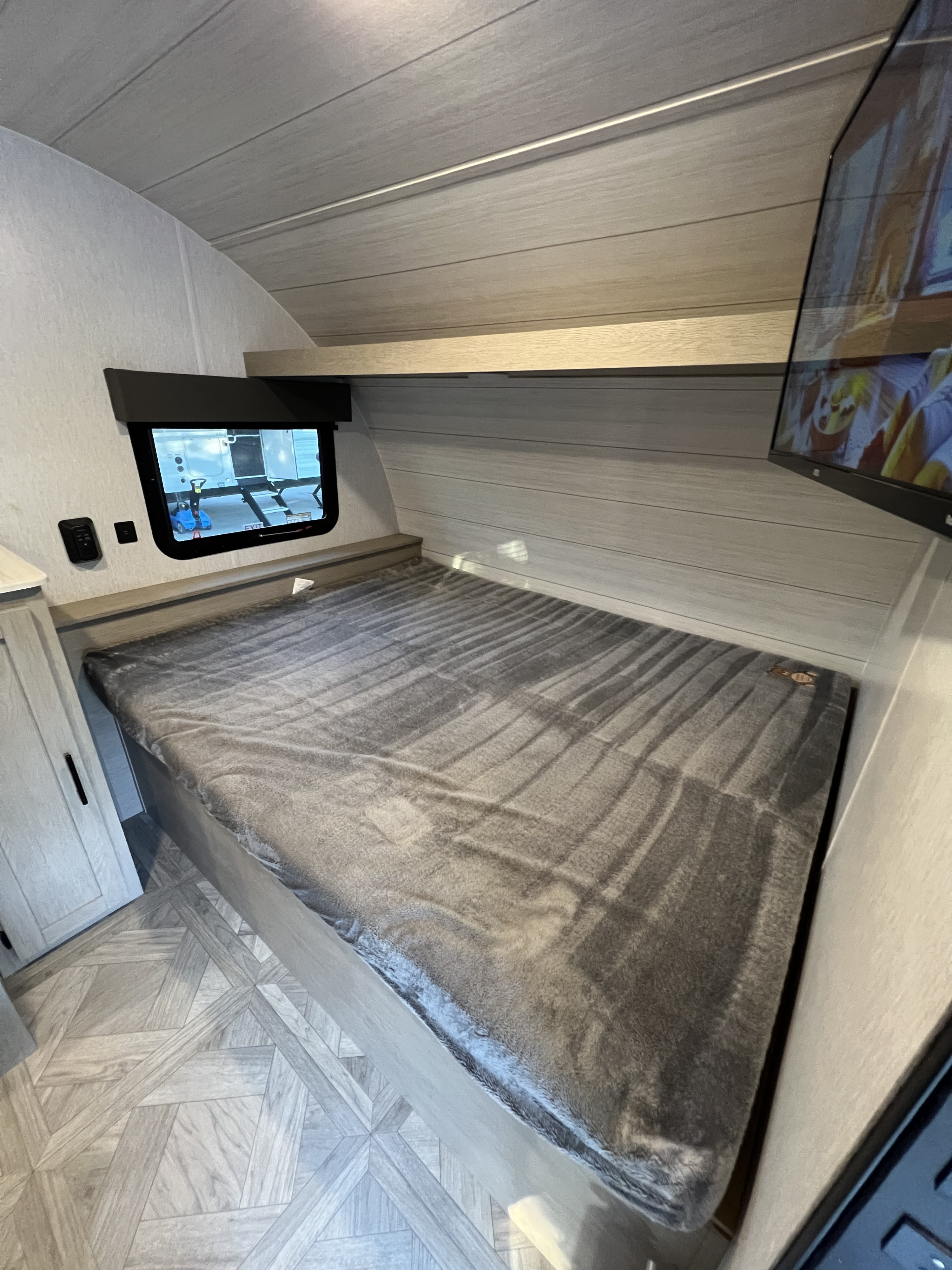 Spacious RV rental bedroom with a cozy grey blanket on the bed, light wood-paneled walls, and a mounted TV.. Forest River Salem Cruise Lite 2023
