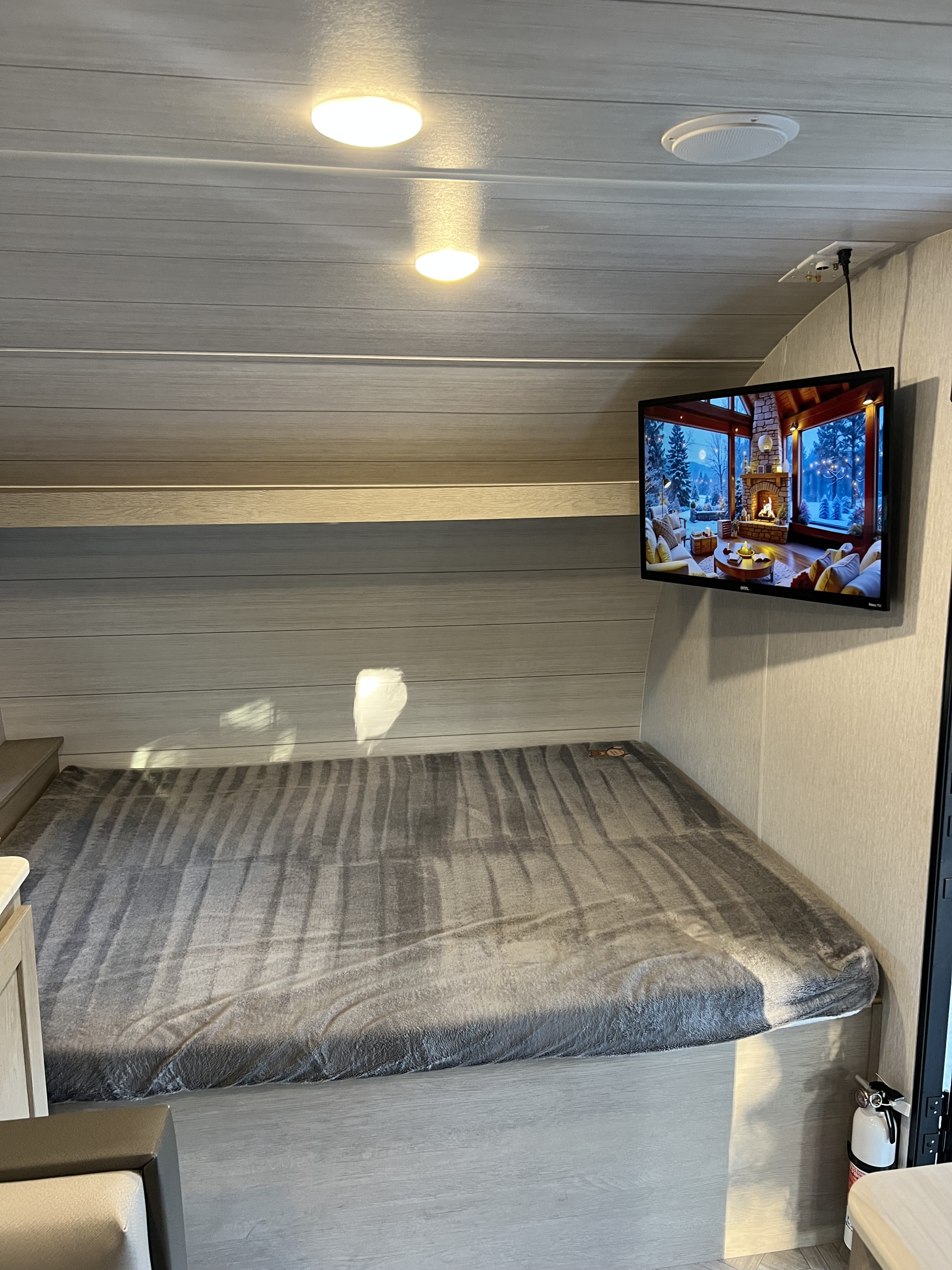 This RV rental's cozy bedroom features a comfortable bed, a wall-mounted TV showing a winter scene, and bright ceiling lights.. Forest River Salem Cruise Lite 2023
